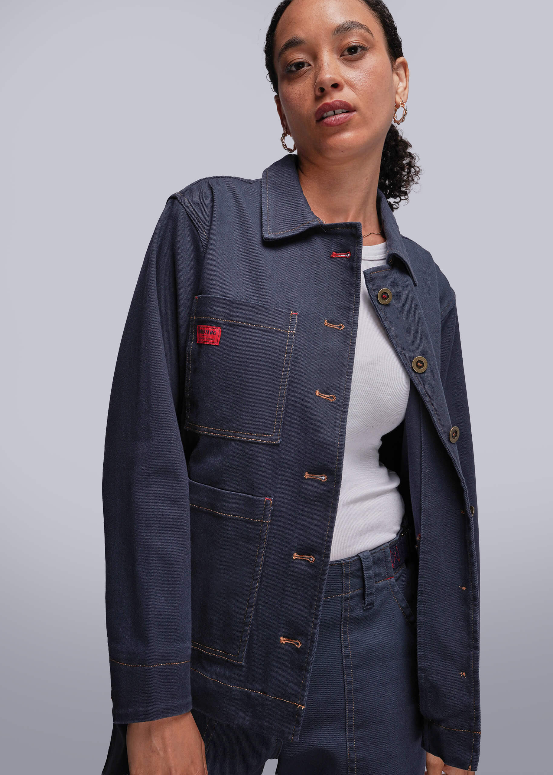 S=Person wearing a dark blue jean jacket with a red label on a light gray background