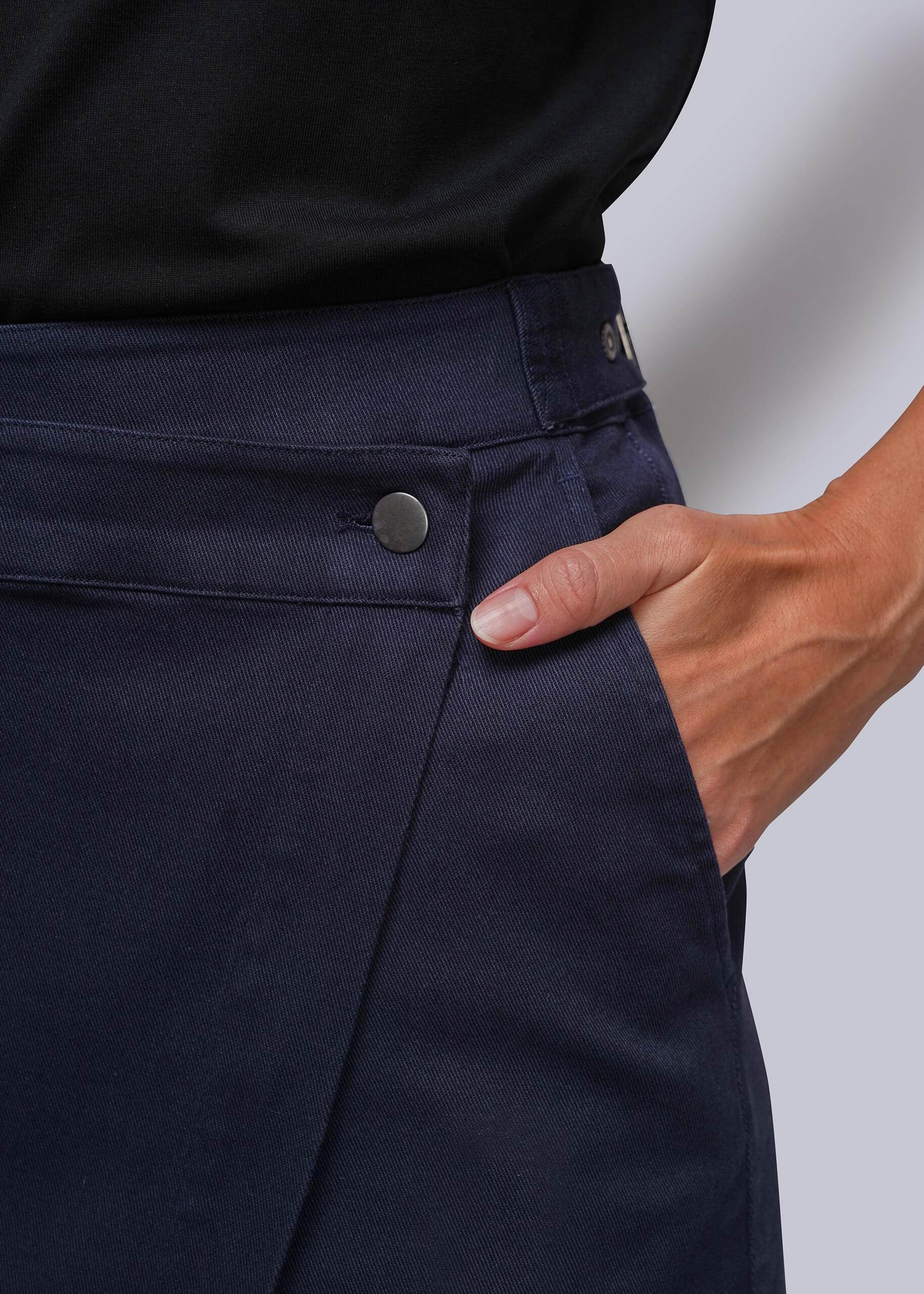 Close-up of a person wearing dark navy wrap skirt, showing the waistband, button closure, side pocket, and hand in the pocket. A black top is also visible at the top edge.