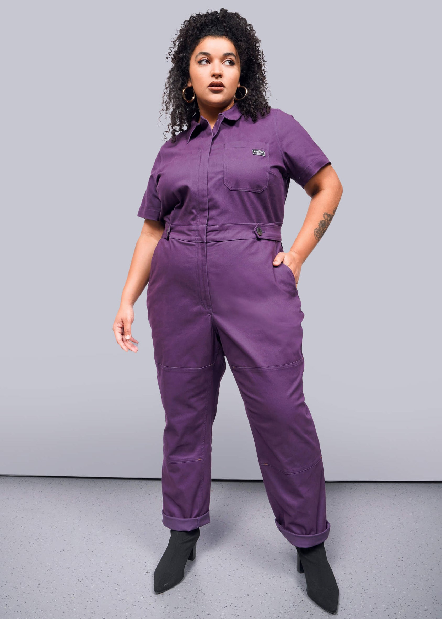 1X=Person wearing a purple jumpsuit against a gray background