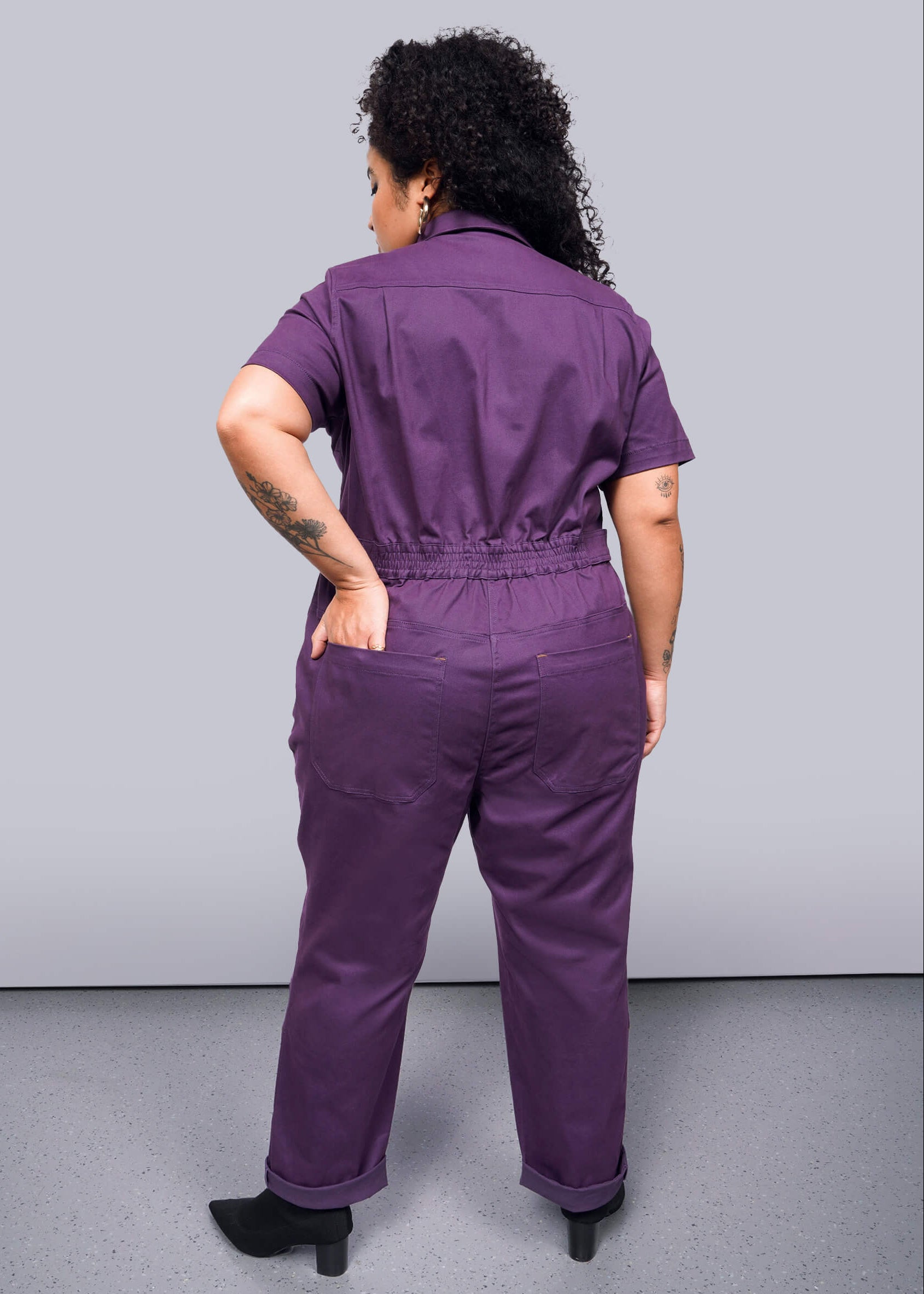 1X=Person wearing a purple jumpsuit against a gray background
