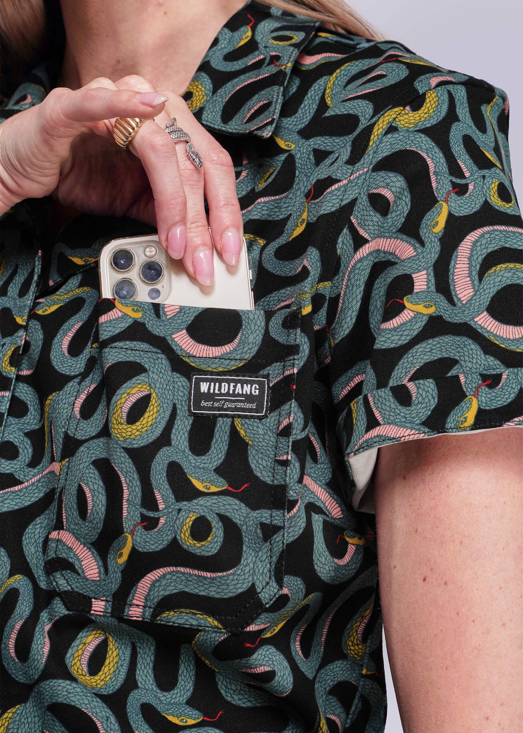 Person wearing a patterned shirt with a visible brand label, holding a phone.