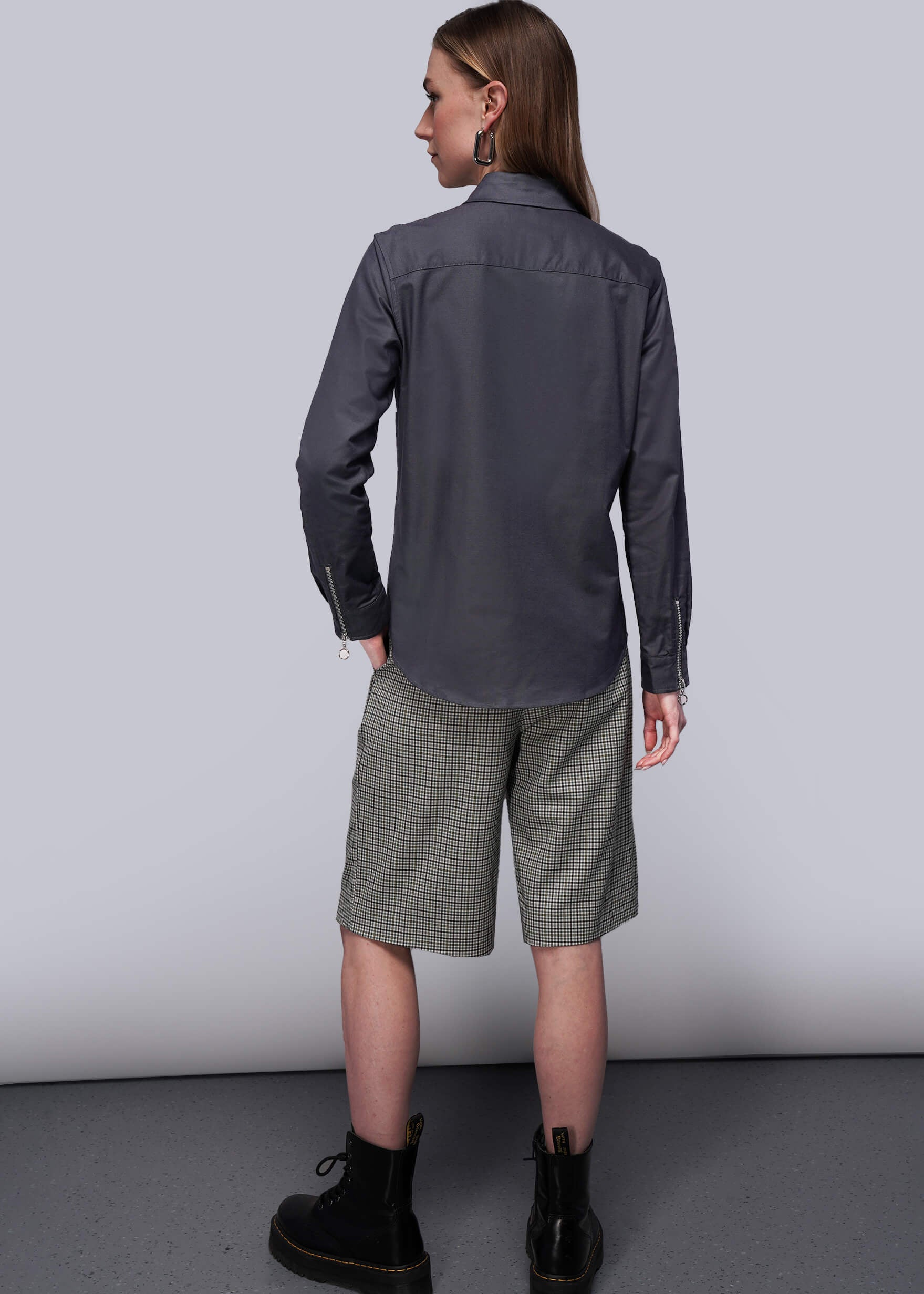 S=Person wearing a black shirt and plaid shorts standing against a plain background