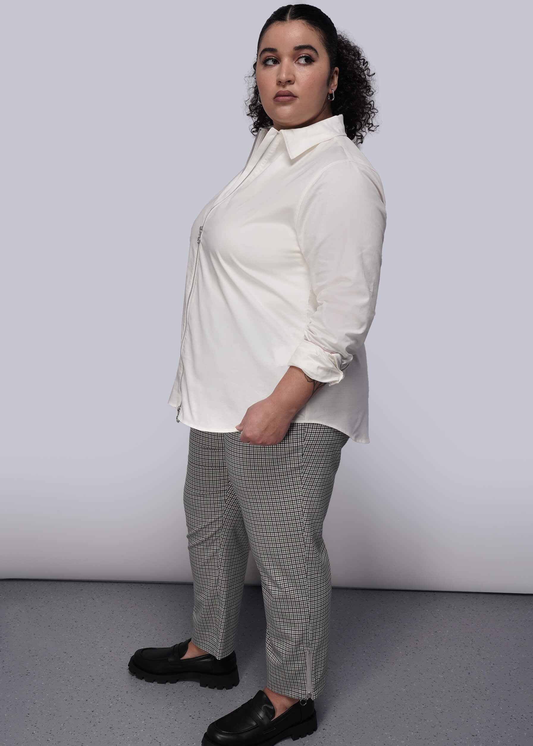 1X=Side view of person wearing a white shirt with zipper and checkered pants against a plain background