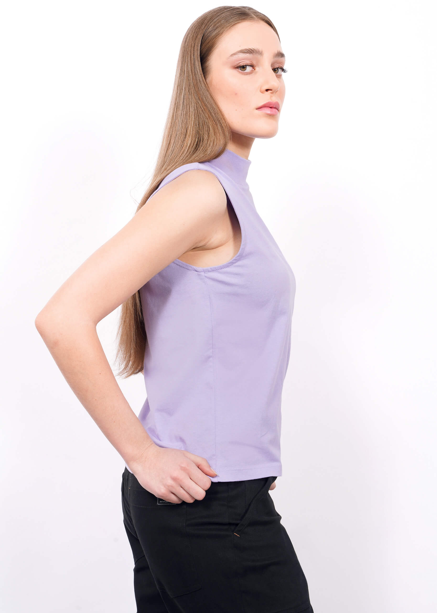S=A woman with long straight hair models The Essential Mock Neck Tank in lavender and black pants, standing in a side profile pose against a plain white background.