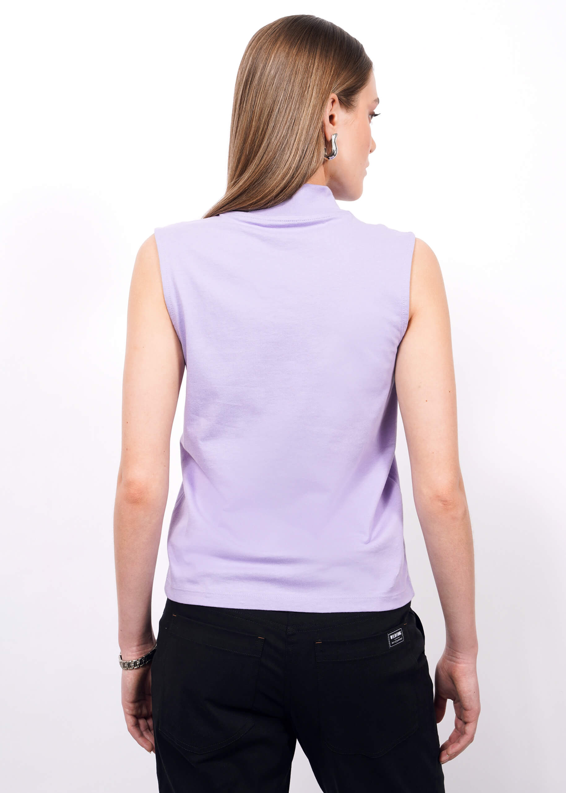 S=A person with straight, long light brown hair is shown from the back, wearing The Essential Mock Neck Tank in light purple and black pants, standing against a plain white background.