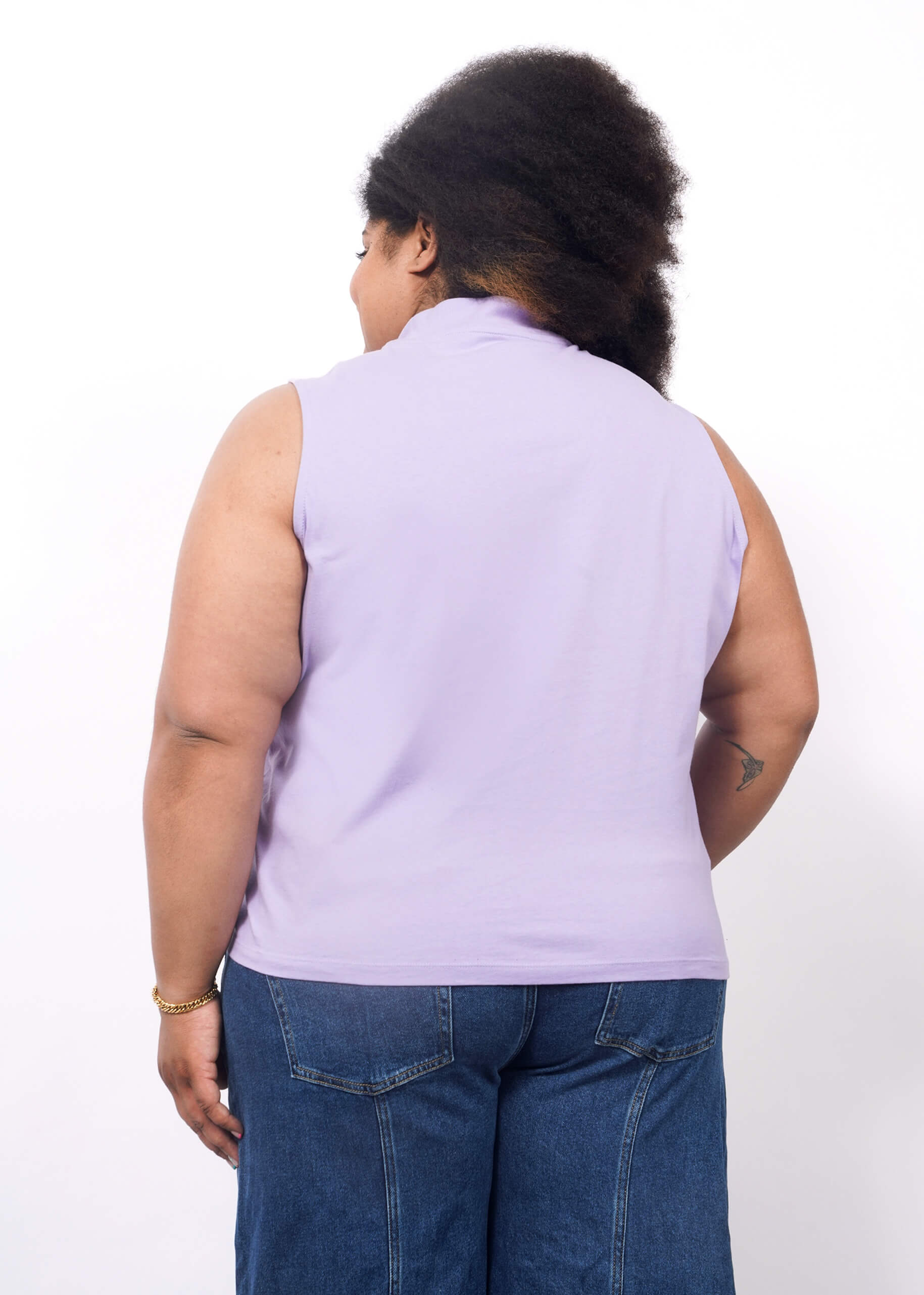1X=A person with dark, curly hair wears The Essential Mock Neck Tank in lavender and blue jeans, standing with their back to the camera against a plain white background.
