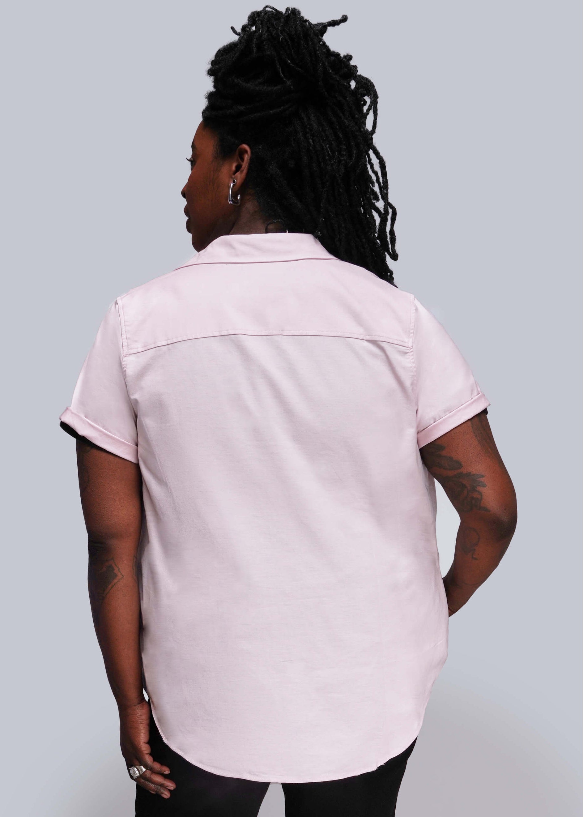 1X=Person wearing a light pink short-sleeve shirt against a gray background