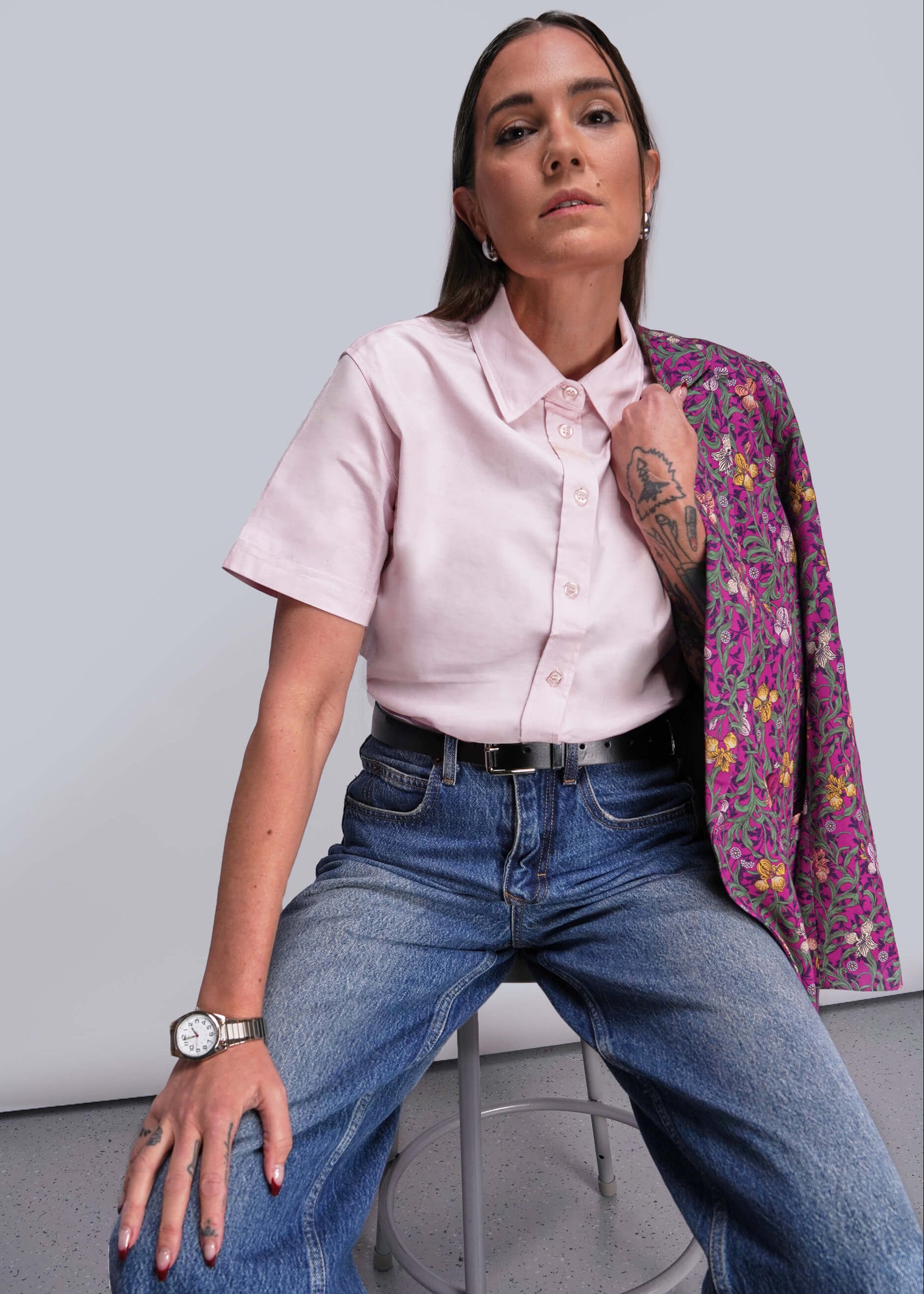 S=Person wearing a pink shirt, floral jacket, and blue jeans against a plain background