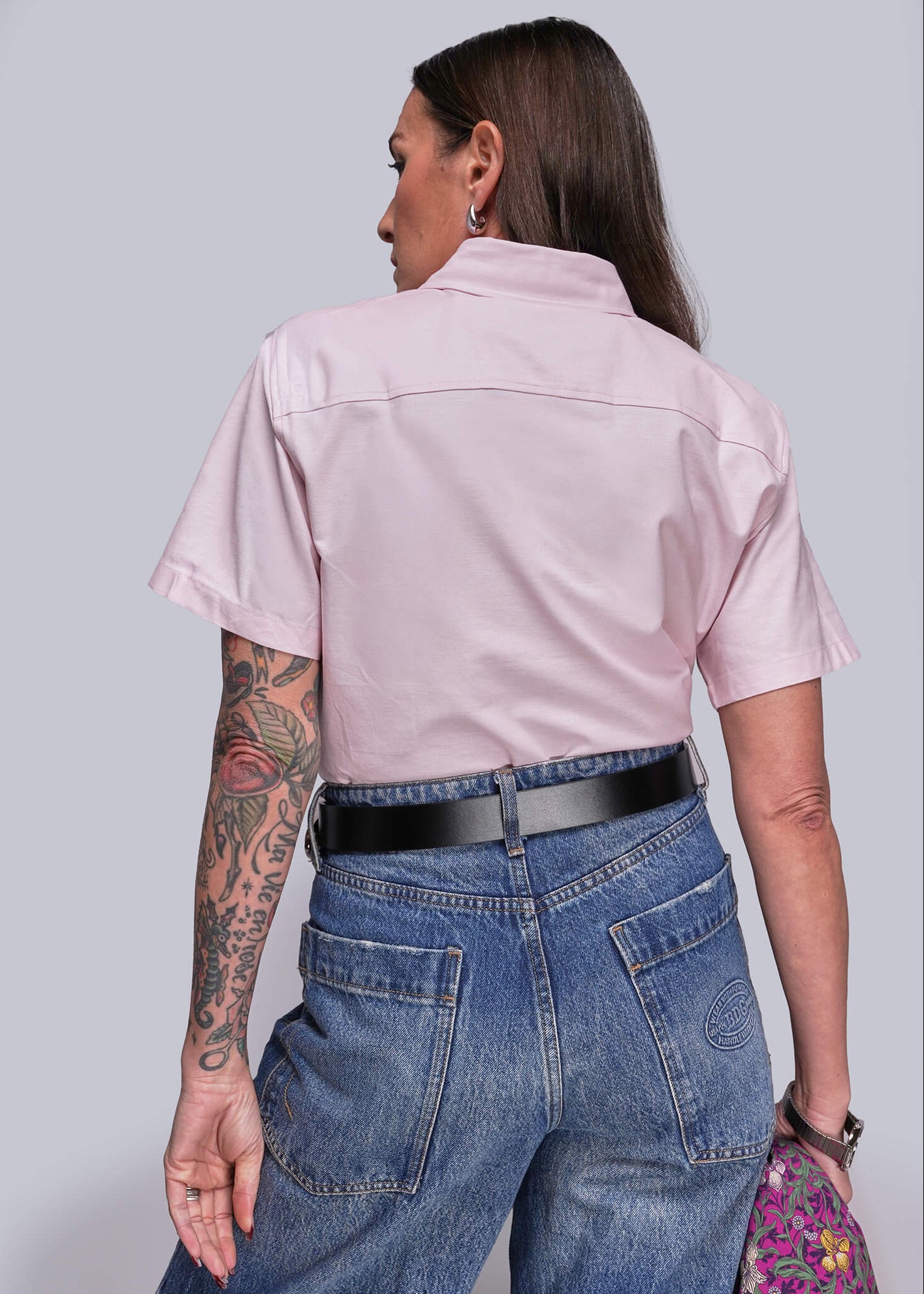 S=Person wearing a light pink shirt and blue jeans against a gray background