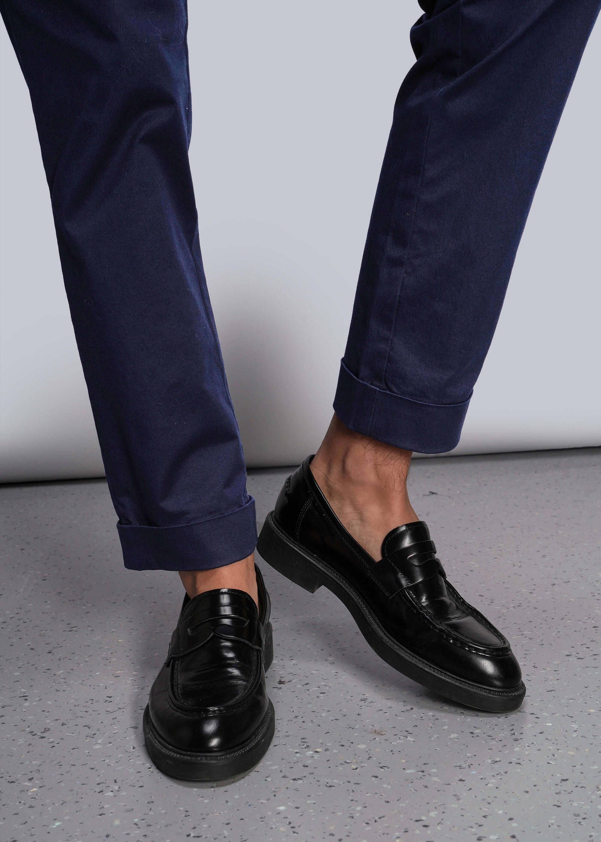 S=Black dress shoes worn with navy pants on a light gray background