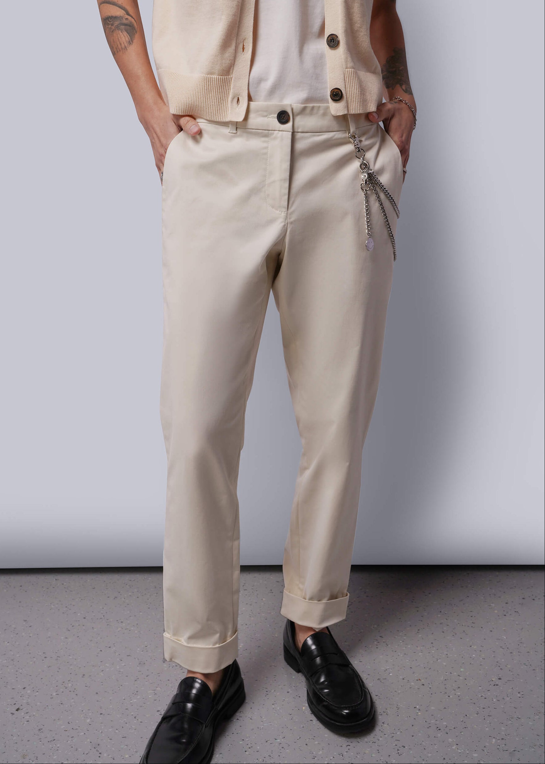 S=Person wearing beige pants and a vest against a plain background
