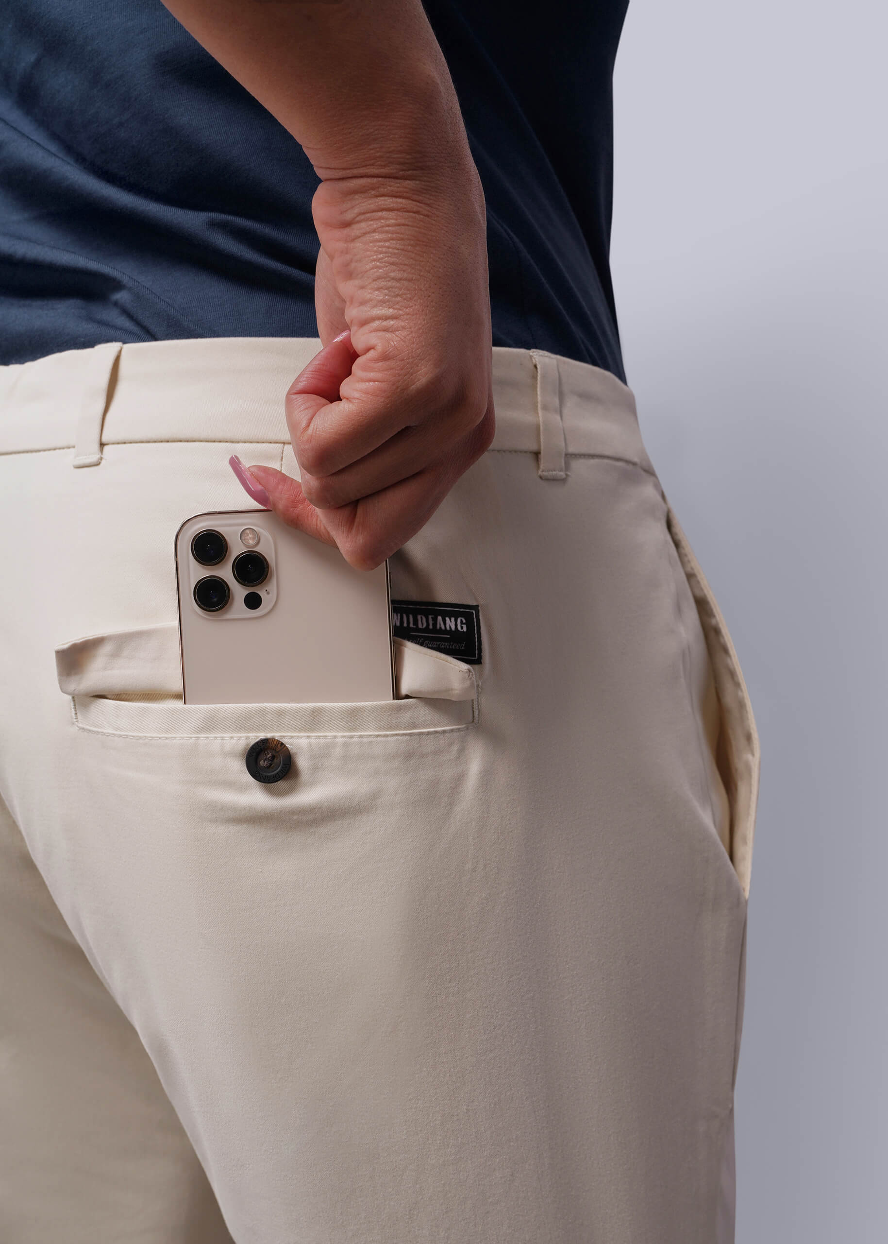 1X=Person wearing beige pants with a phone in the pocket against a plain background