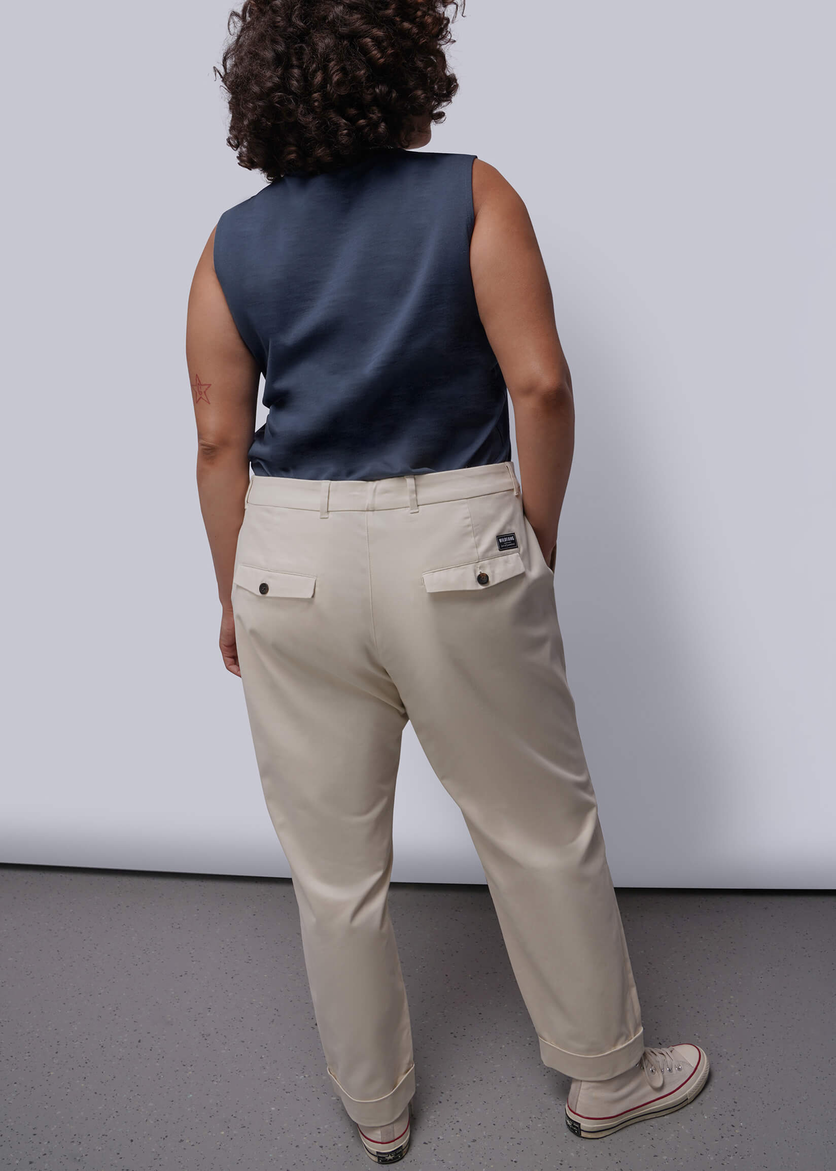 1X=Person wearing a navy sleeveless top and beige pants against a white background