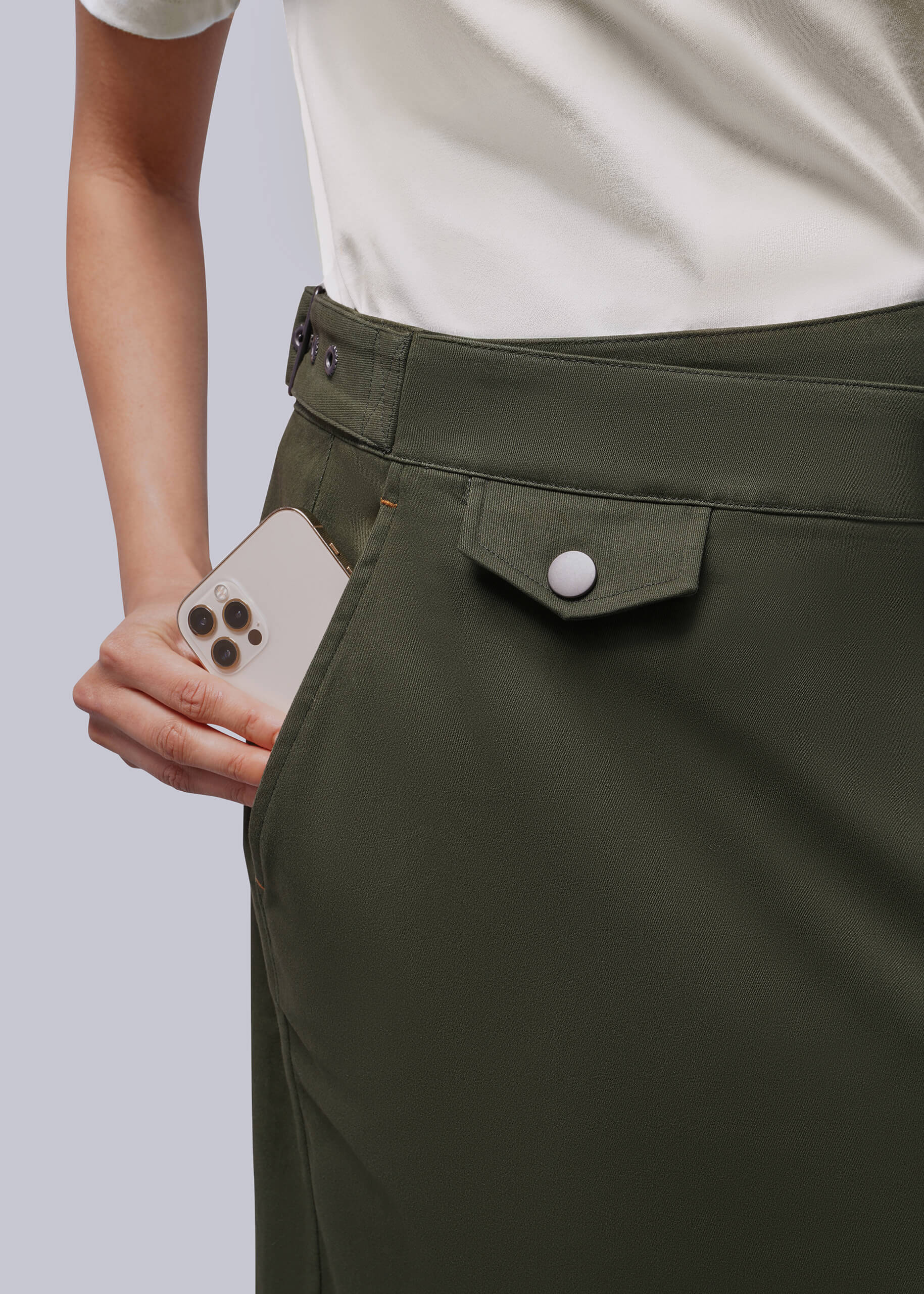 Close up of person placing phone in side pocket of gren skirt