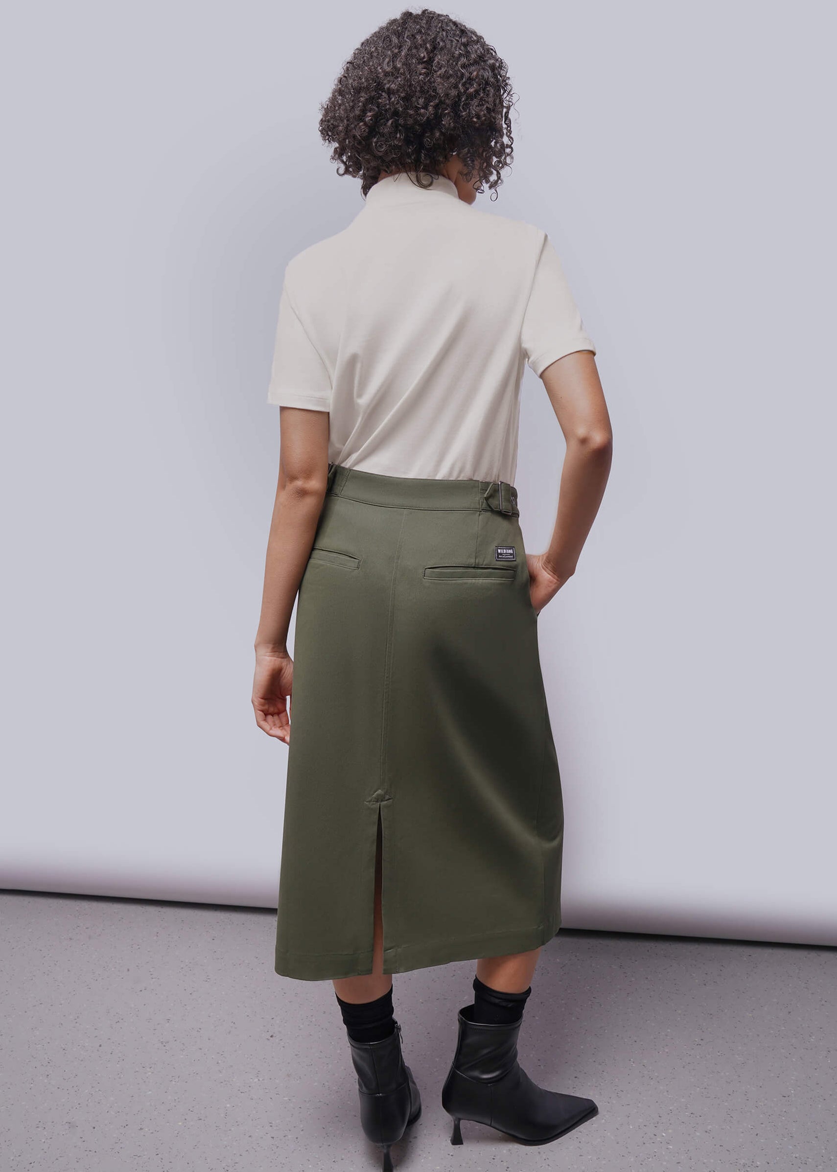 S=Person wearing a beige shirt and green skirt against a white background
