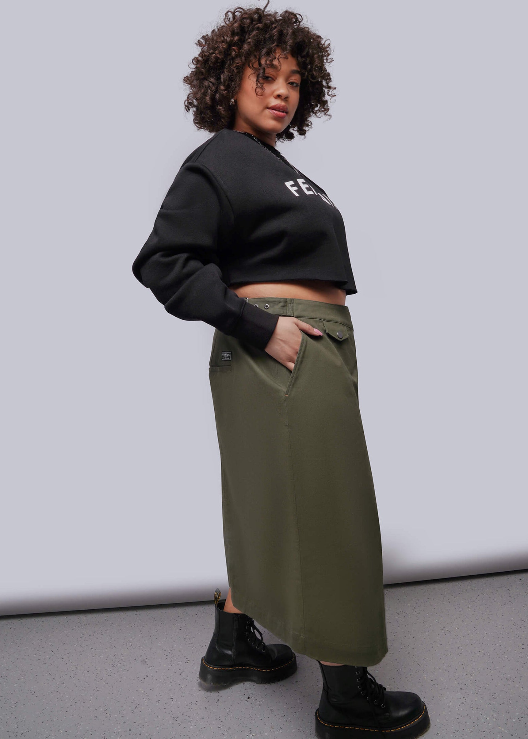 1X=Person wearing a black cropped hoodie and green pants against a plain background