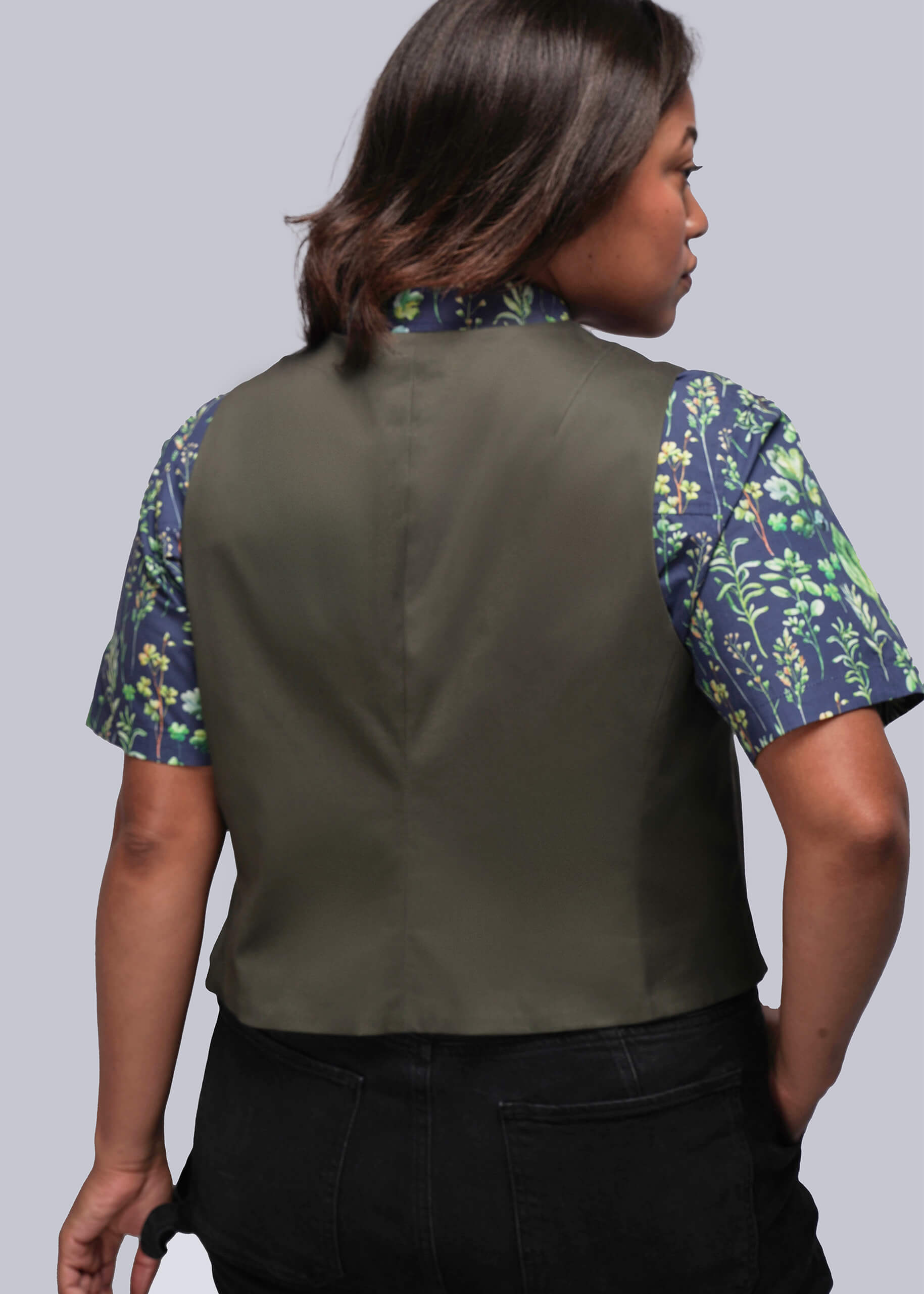 1X=Back view of person wearing a green vest over a leaf print shirt on a plain background