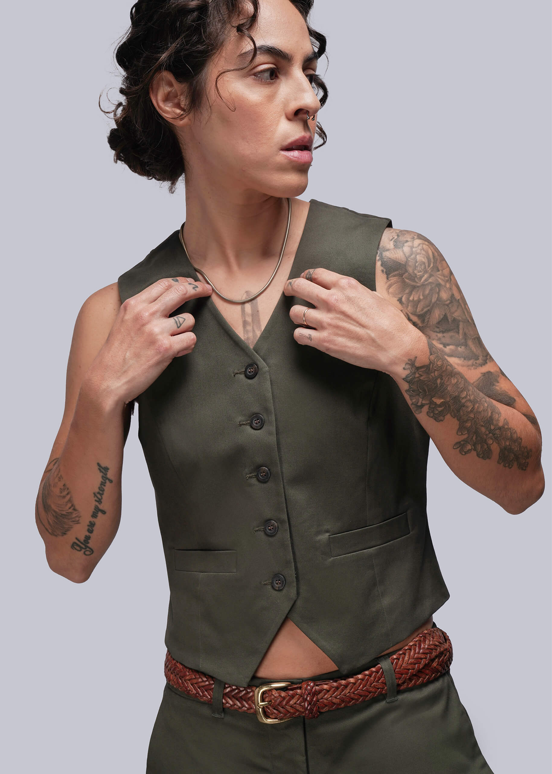 Person wearing a green vest with buttons and a red belt on a plain background