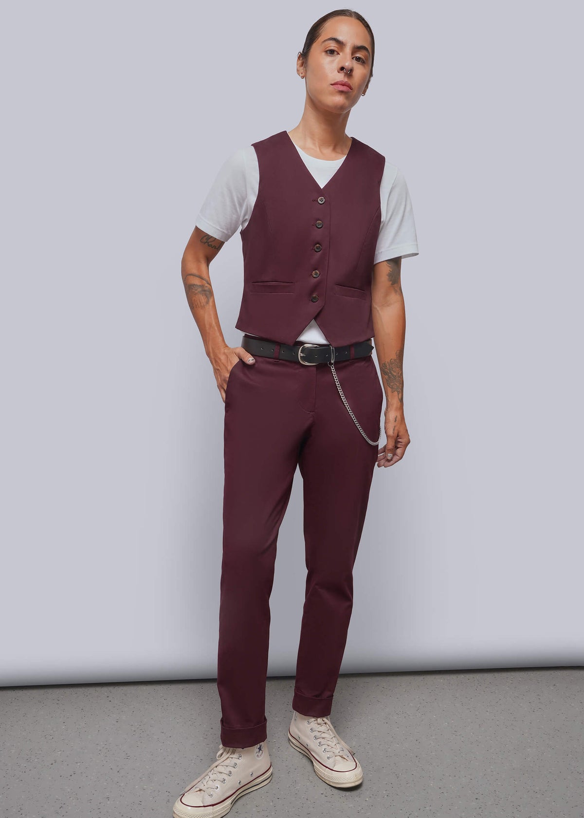 S=A model stands in a studio wearing a burgundy vest and matching trousers with a black belt, layered over a white t-shirt and paired with beige sneakers.