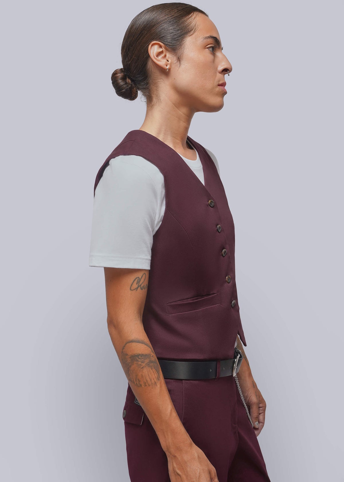 S=A side-profile view of a model wearing a sleeveless maroon vest over a white t-shirt, paired with matching maroon trousers and a black belt, against a solid light gray background.