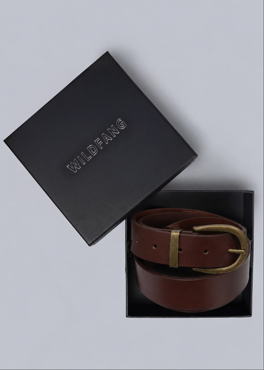 A brown leather belt with a gold buckle, presented in a black box next to its black Wildfang brand lid on a light gray background.