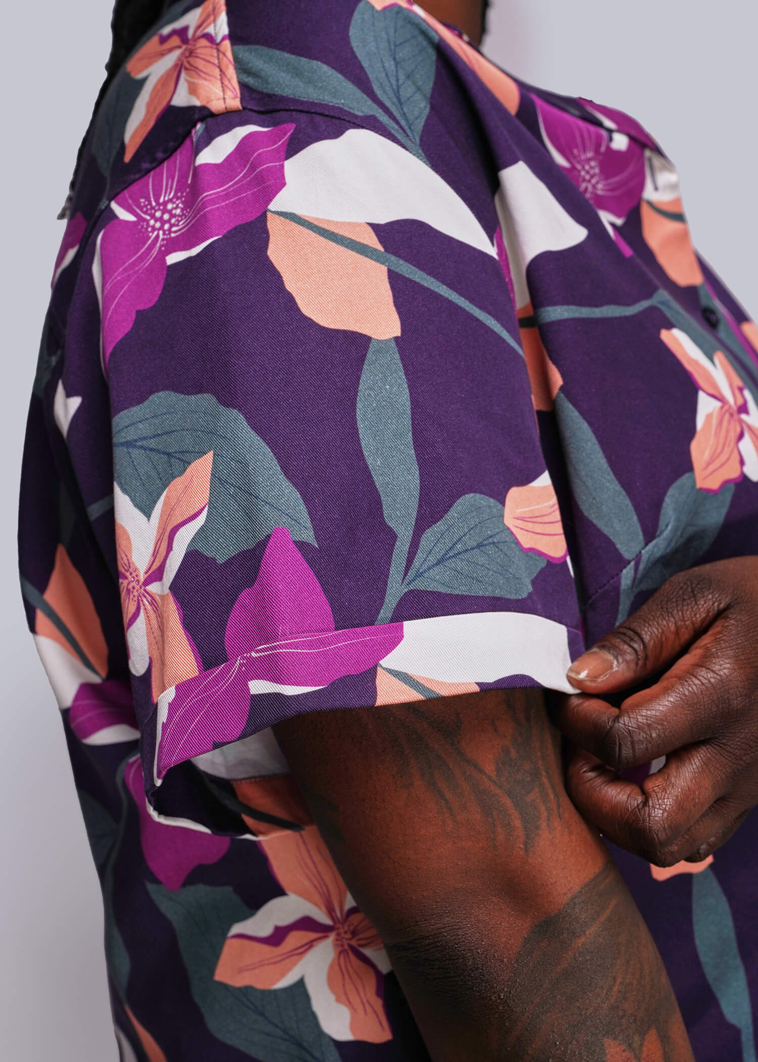 1X=Close-up of a person wearing a floral-patterned garment with a purple background.