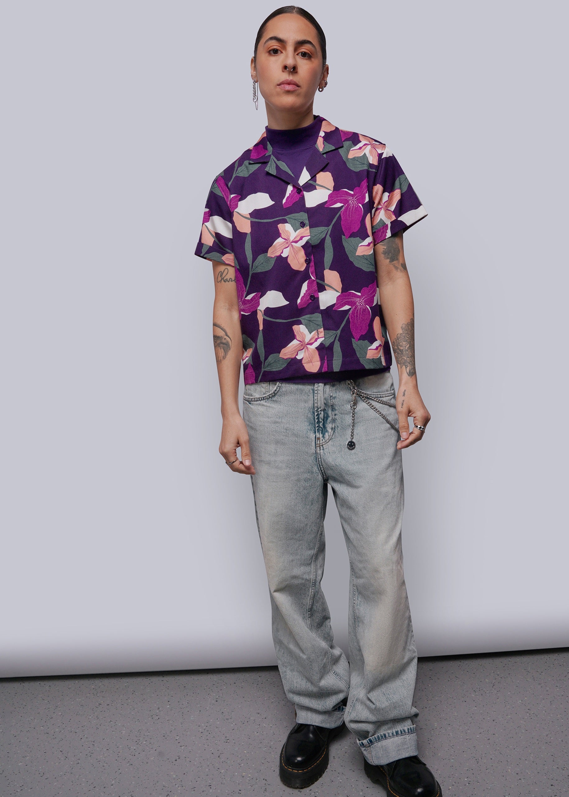 S=Person wearing a purple floral shirt and light gray jeans against a white background