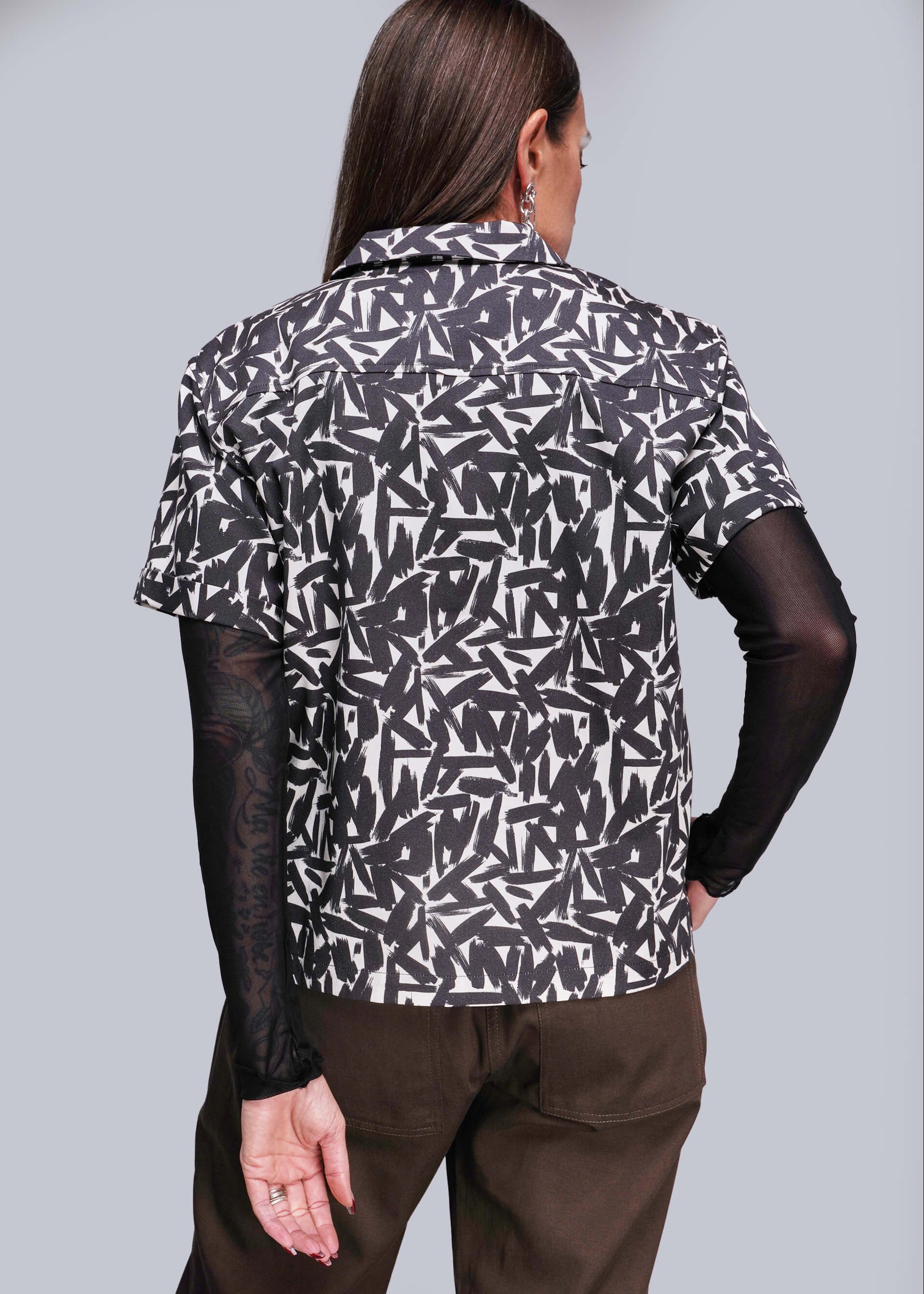 S=Person wearing a patterned shirt with sheer sleeves against a gray background