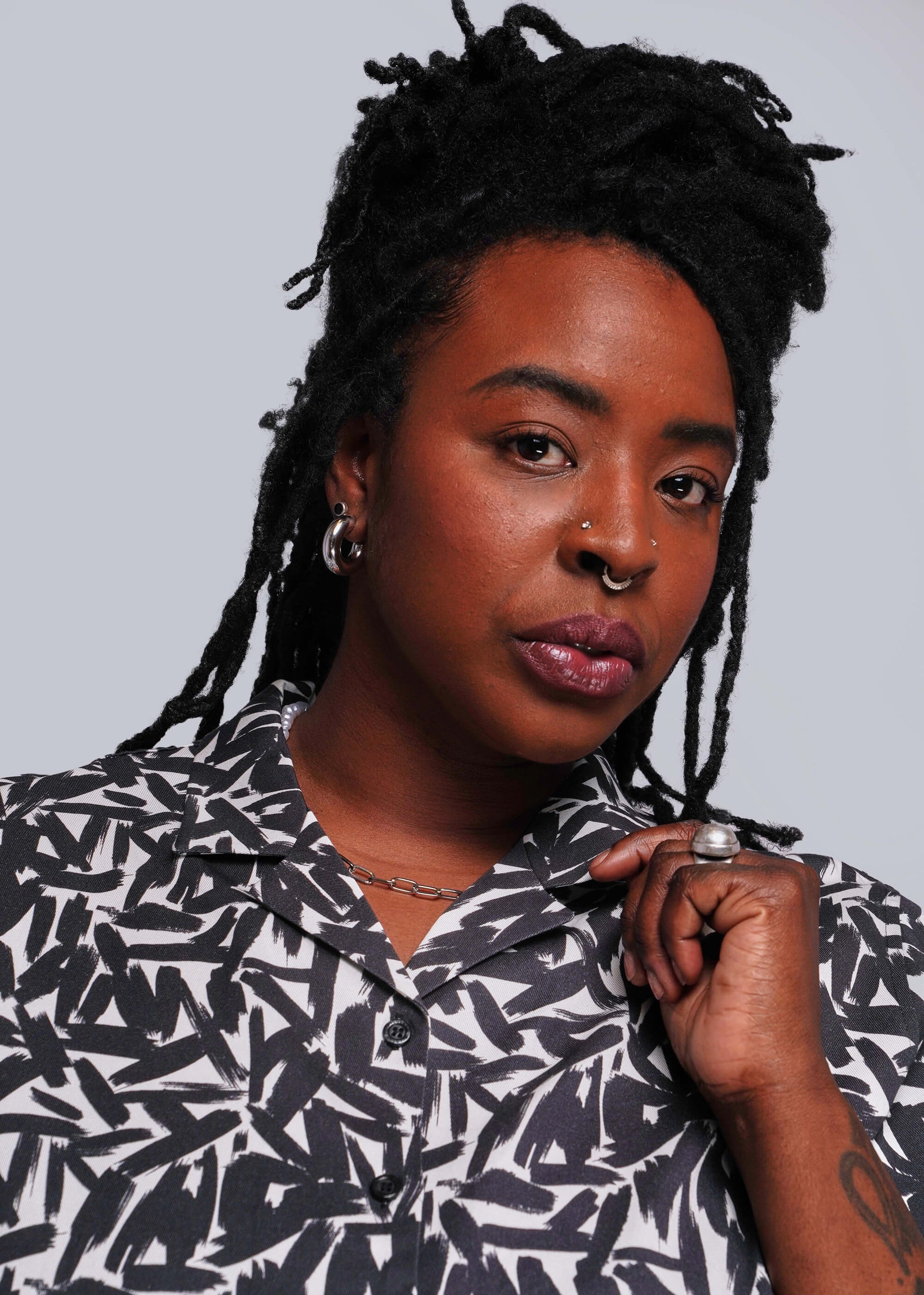 1X=Person with braided hair wearing a black and white patterned shirt against a gray background