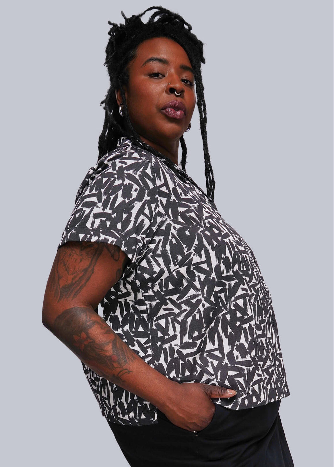 1X=Person wearing a patterned shirt and black skirt against a plain background