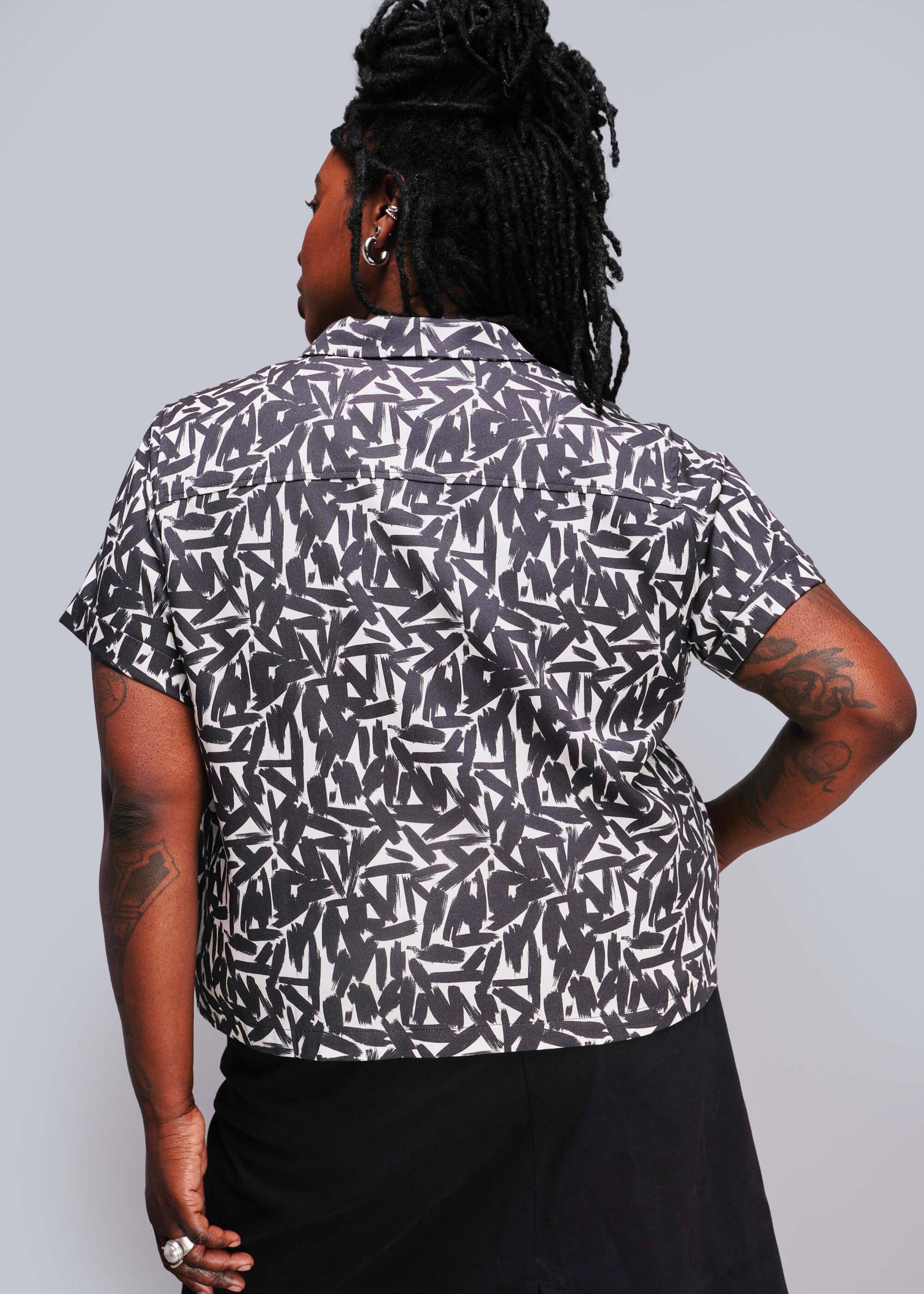 1X=Person wearing a black and white patterned shirt against a gray background