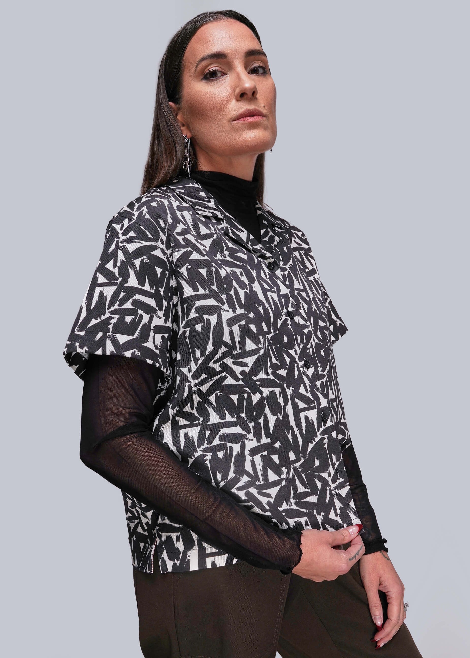 S=Woman wearing a black and white patterned top with sheer sleeves against a gray background