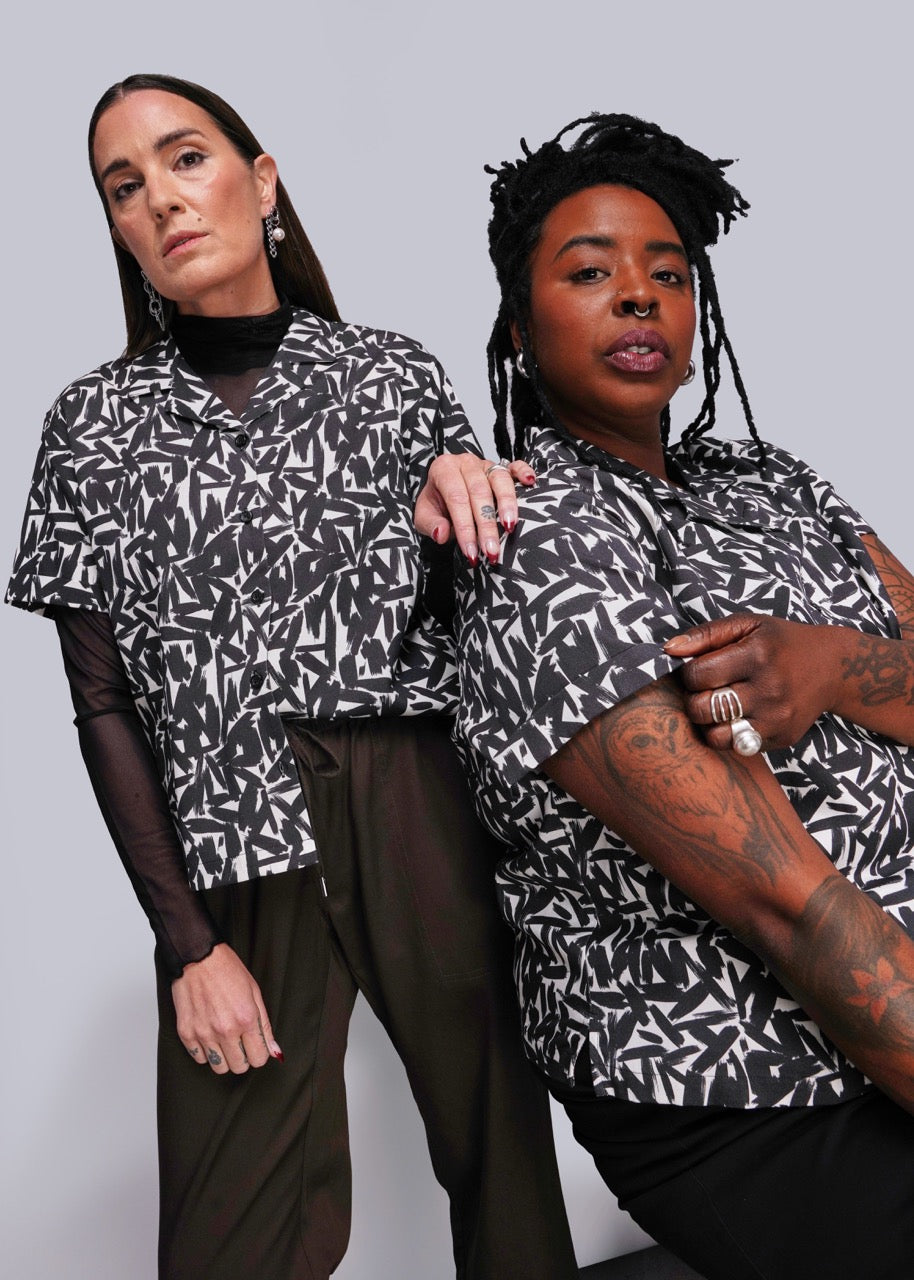Two women wearing black and white patterned tops against a plain background