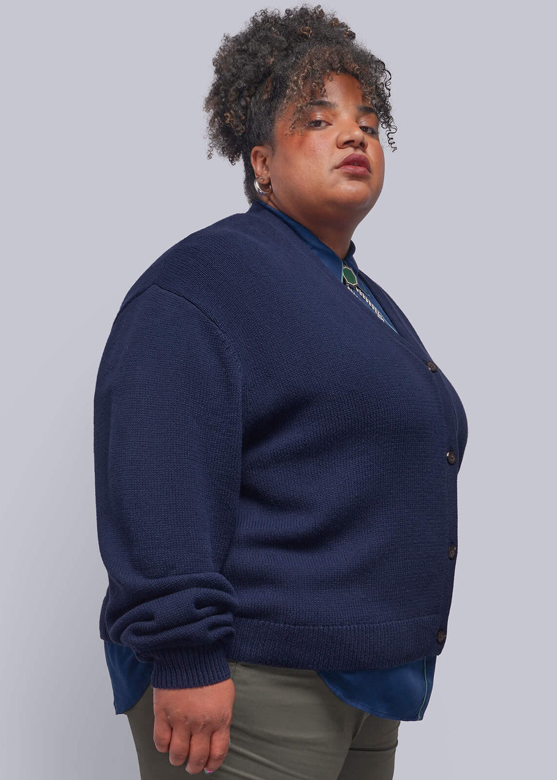 1X=A person modeling a navy blue quarter-zip sweatshirt, olive green pants, and black loafers against a plain light gray studio background.