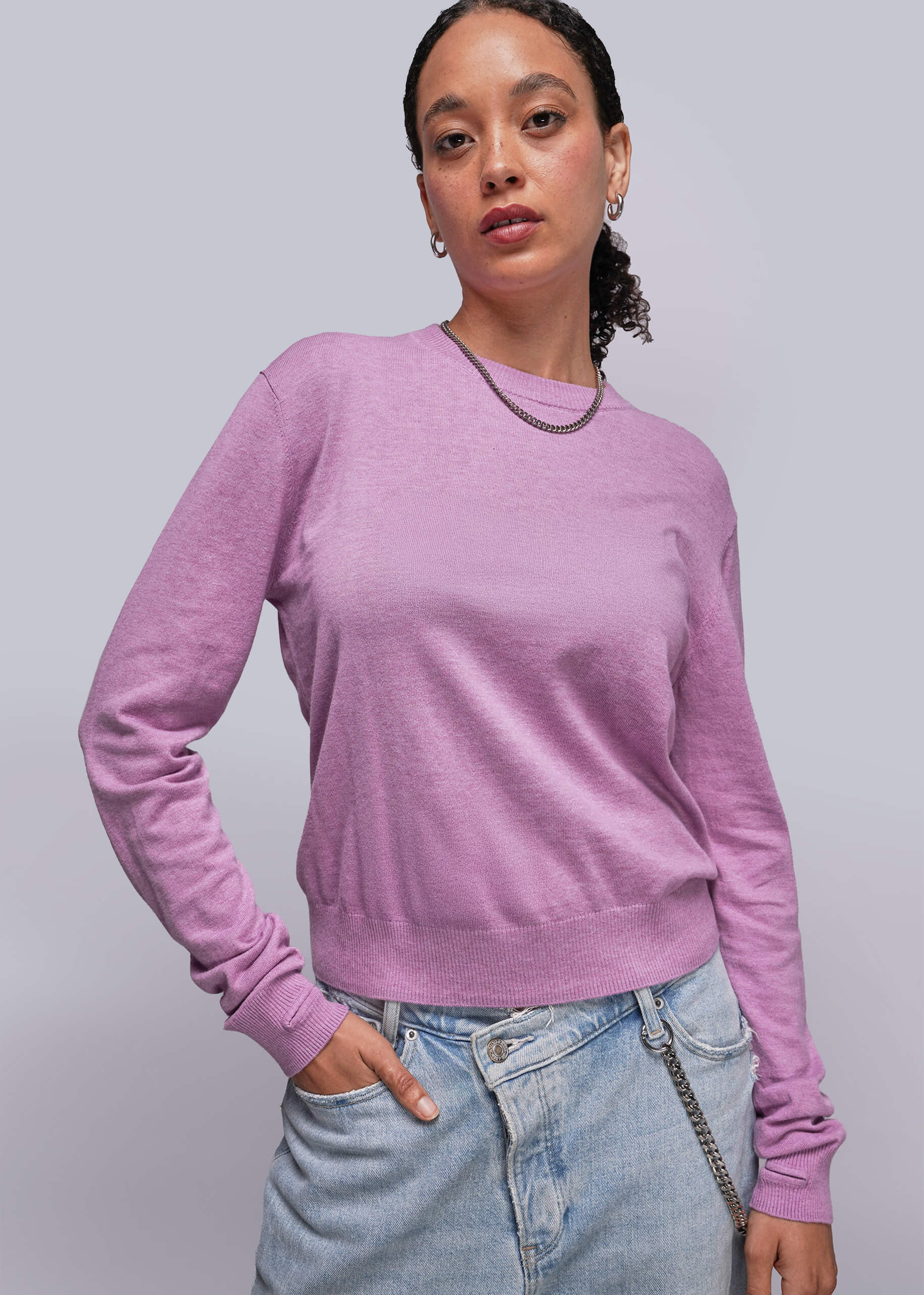 S=Person wearing a pink sweater and light blue jeans against a plain background