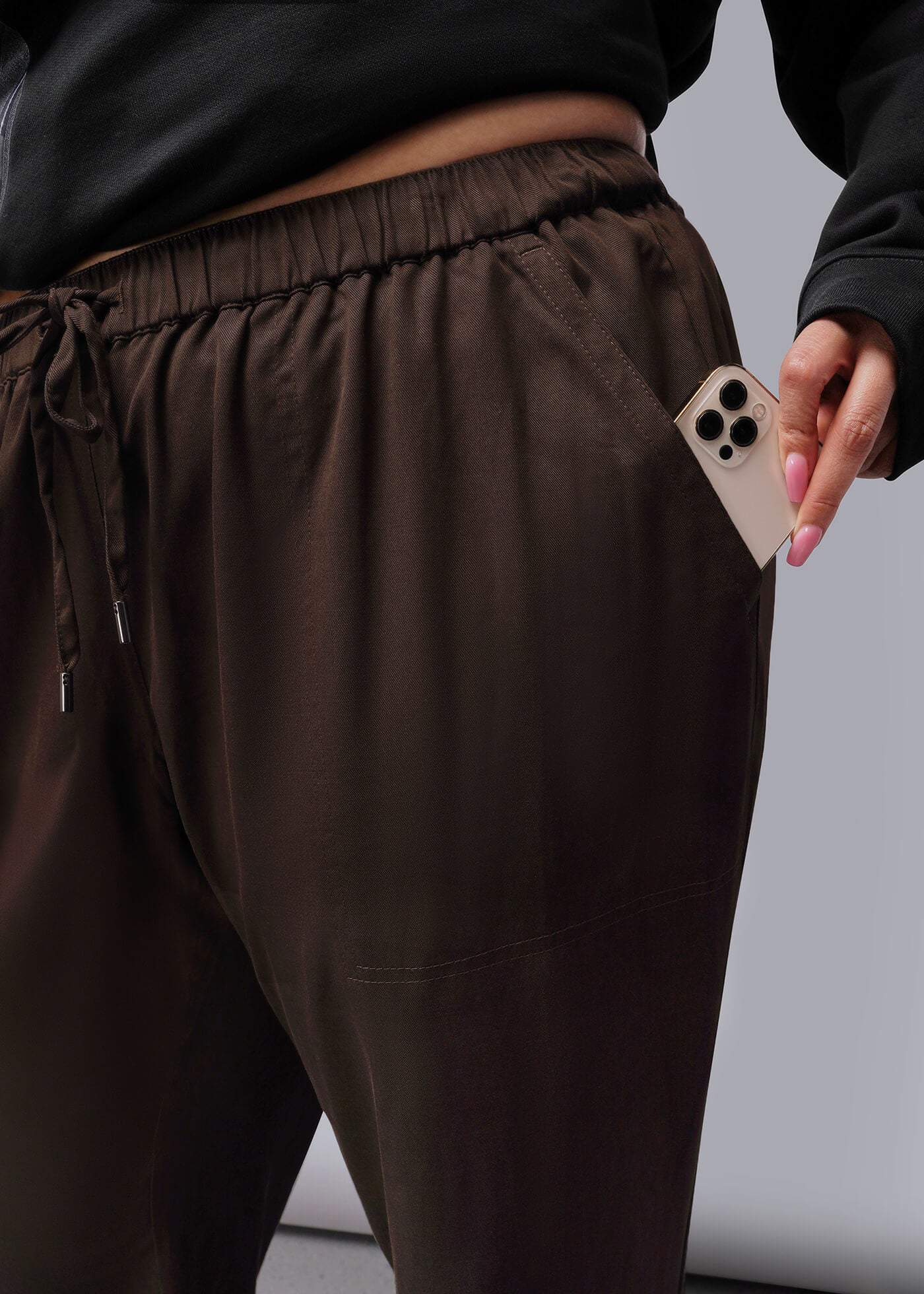 1X=Person wearing brown pants holding a phone with a gray background