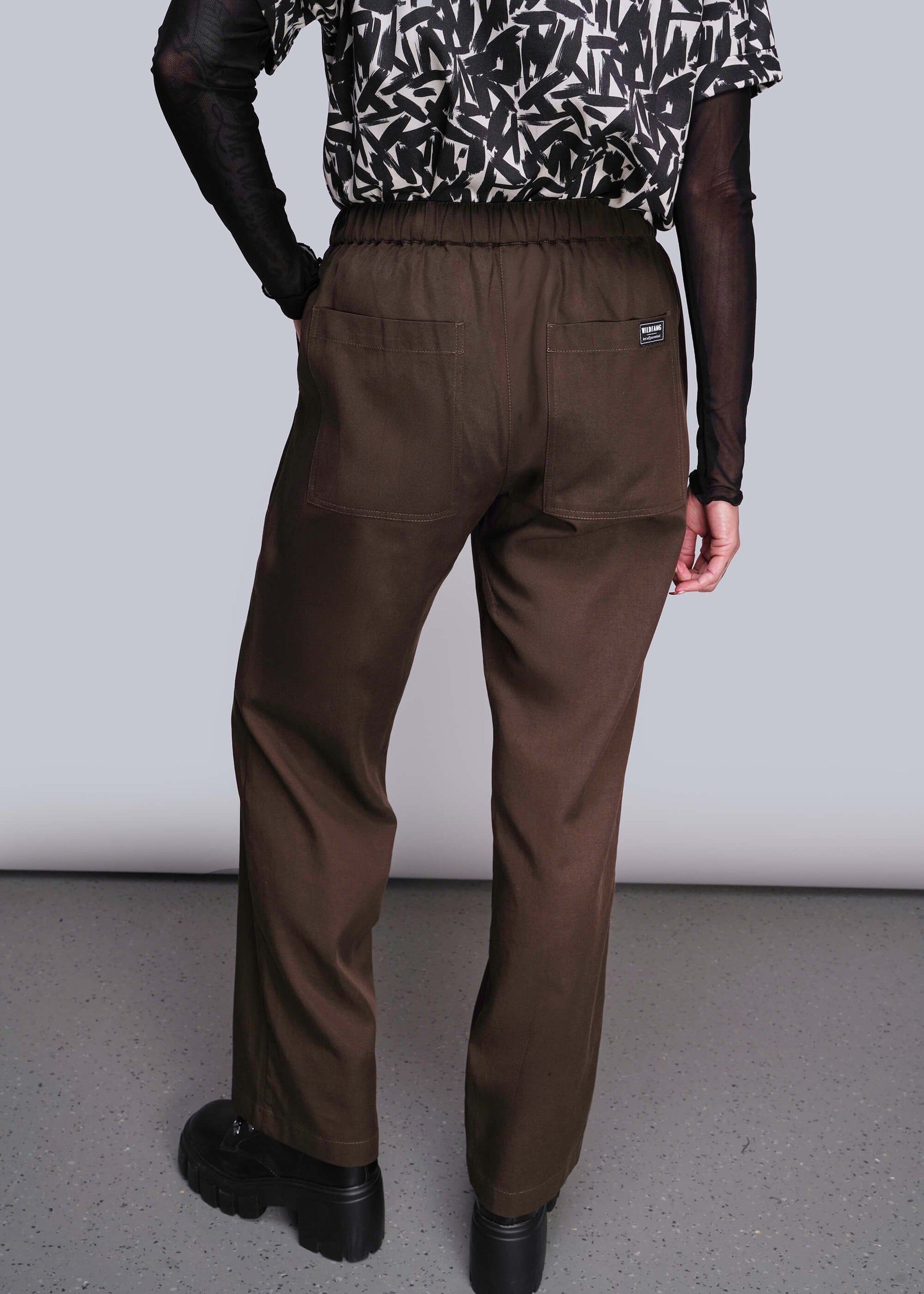 S=Person wearing brown pants and a patterned top on a plain background