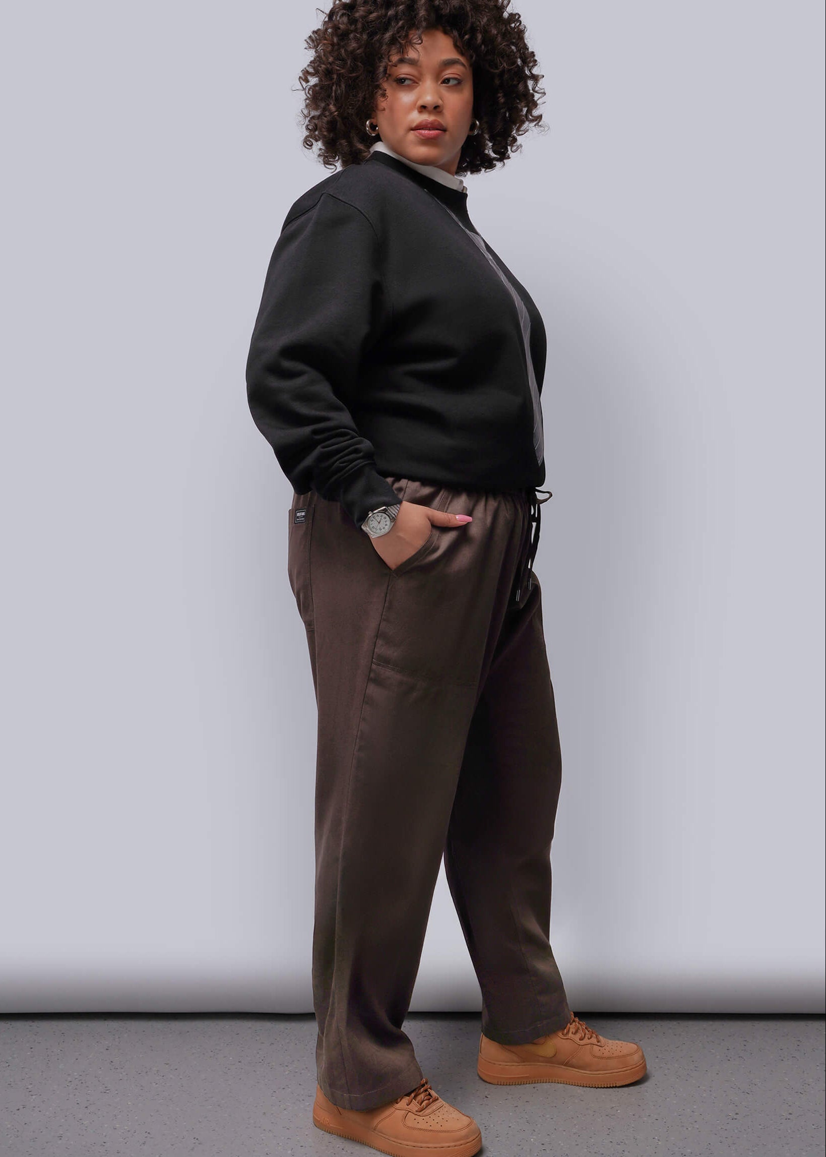 1X=Person wearing a black sweater and brown pants against a white background