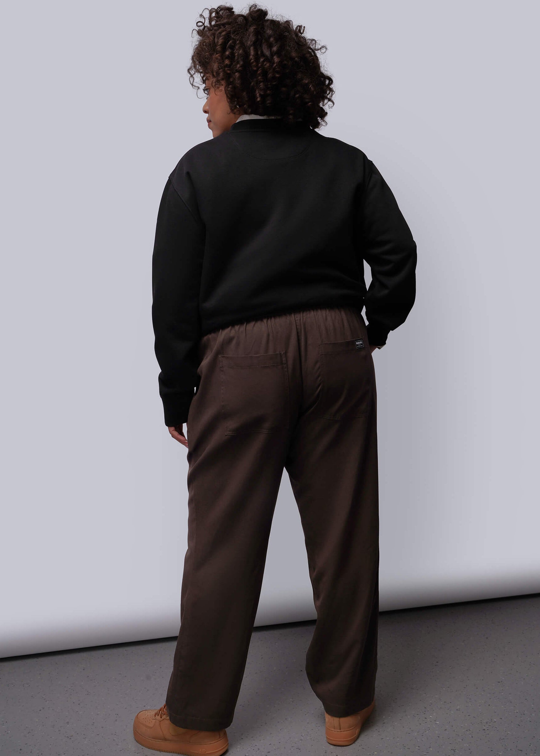 1X=Person wearing a black sweater and brown pants against a white background