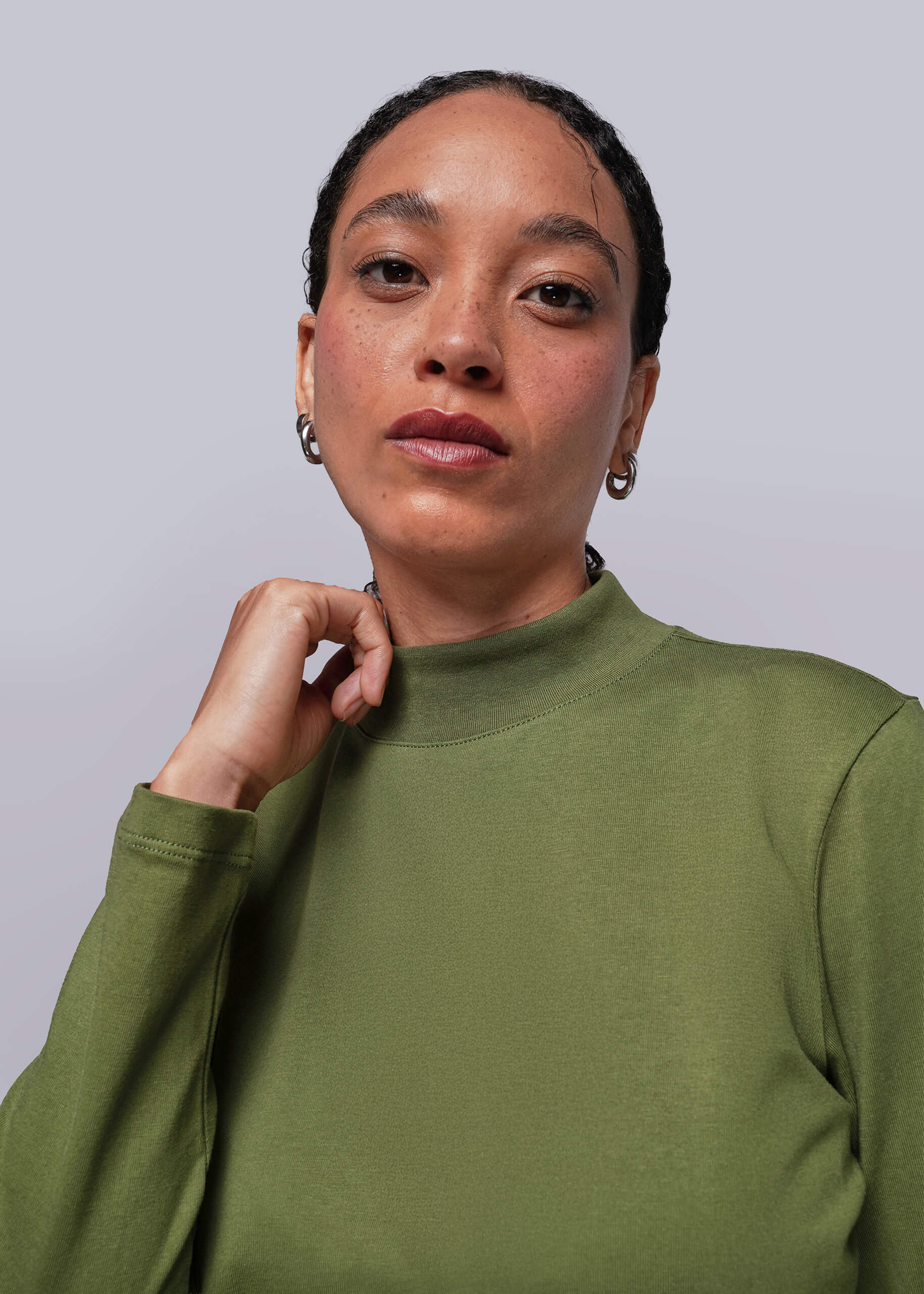 S=Person wearing a green long sleeve shirt holding mock neck collar against a plain background