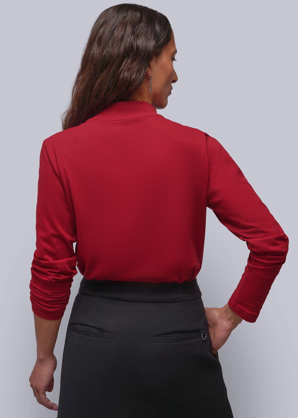 1X=A woman shown from the back wearing a long-sleeve red mock-neck top and a black skirt, standing against a solid light gray background.