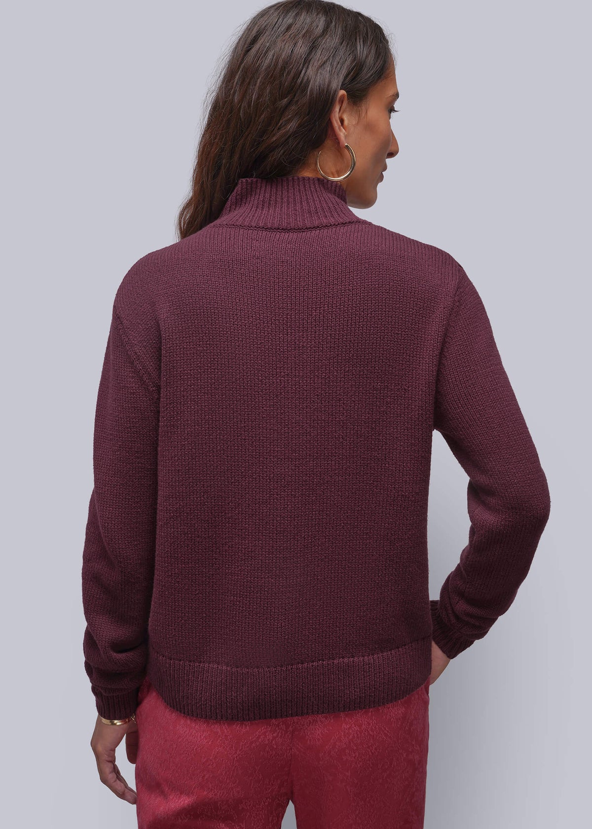 S=A woman shown from the back wearing a ribbed turtleneck sweater in deep burgundy and matching burgundy pants, set against a solid light gray background.
