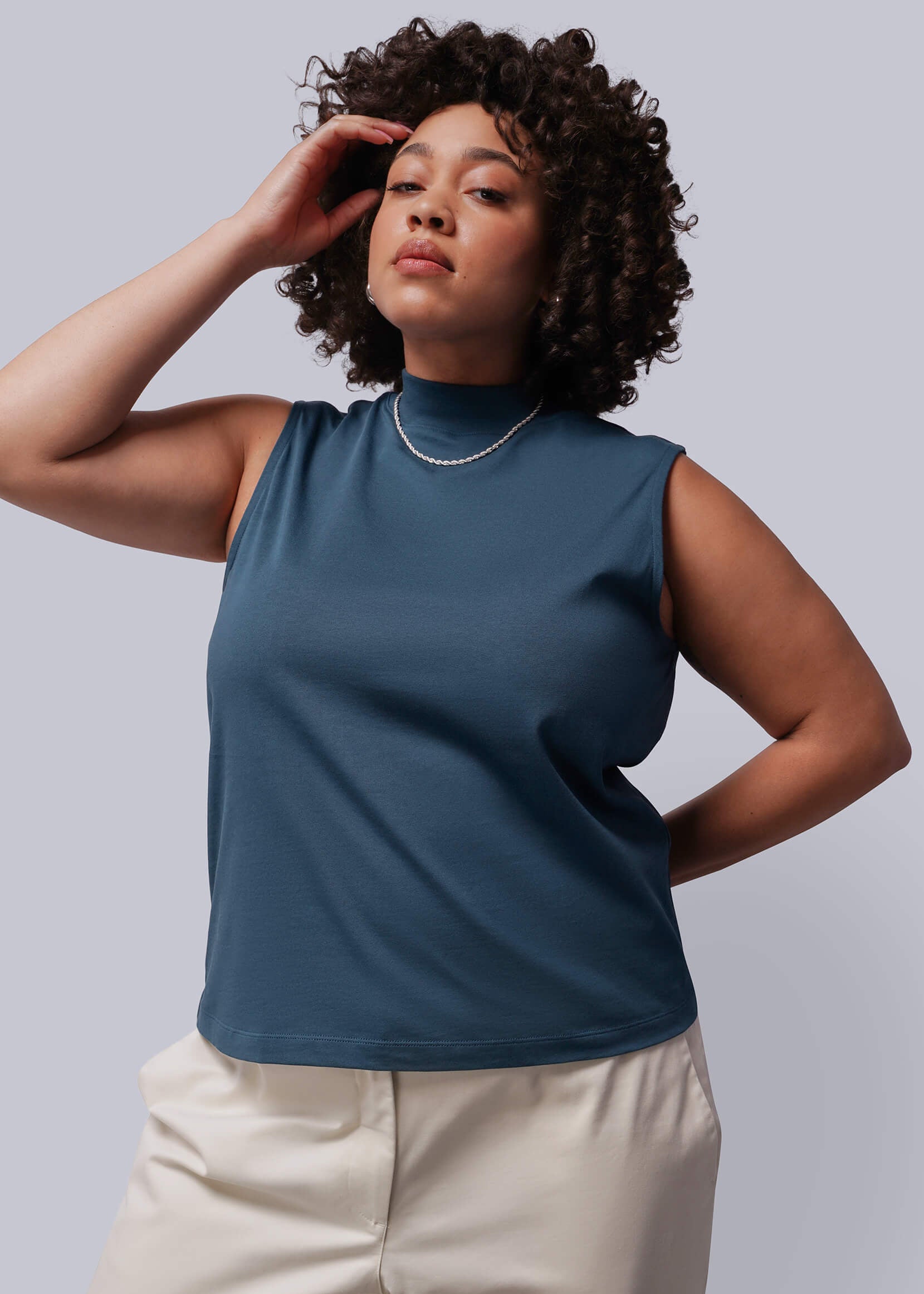 1X=Person wearing a blue sleeveless top and beige pants against a gray background