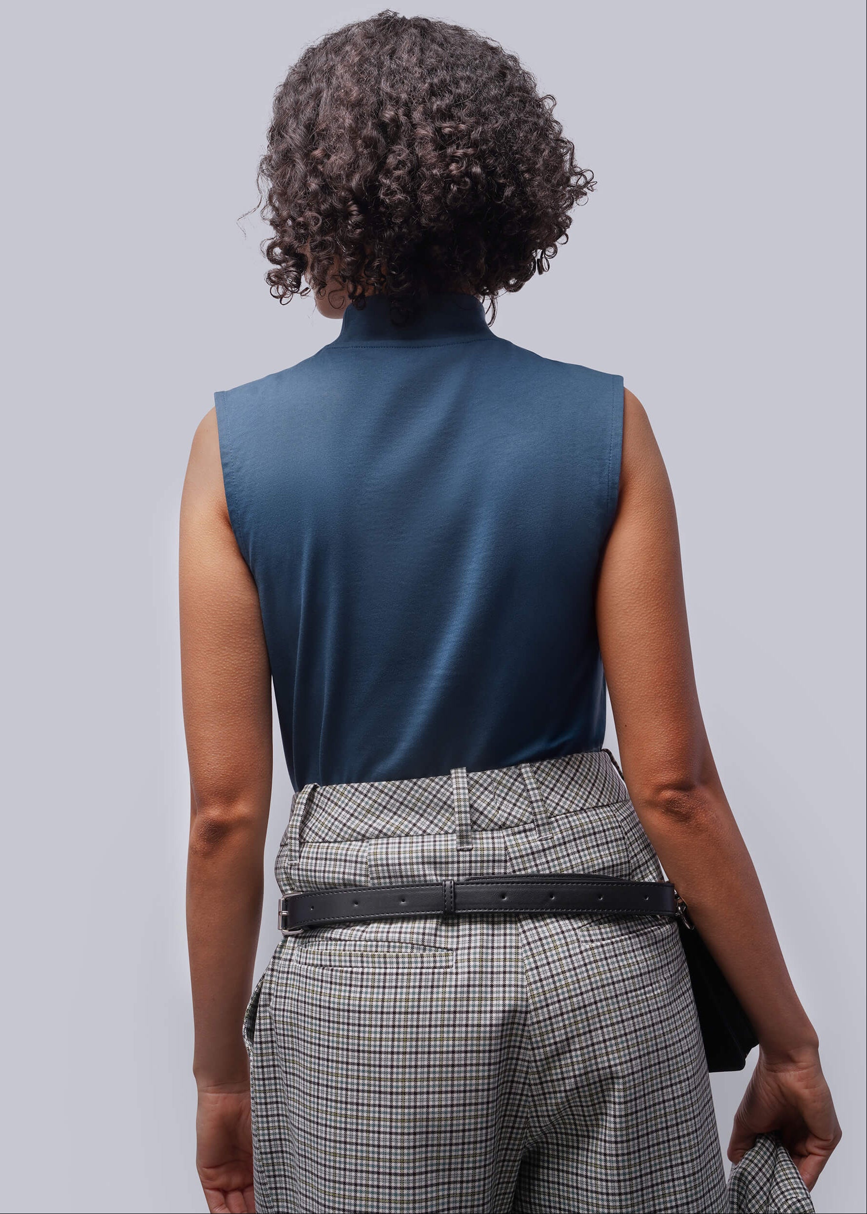 S=Person wearing a blue sleeveless top and plaid pants on a light gray background