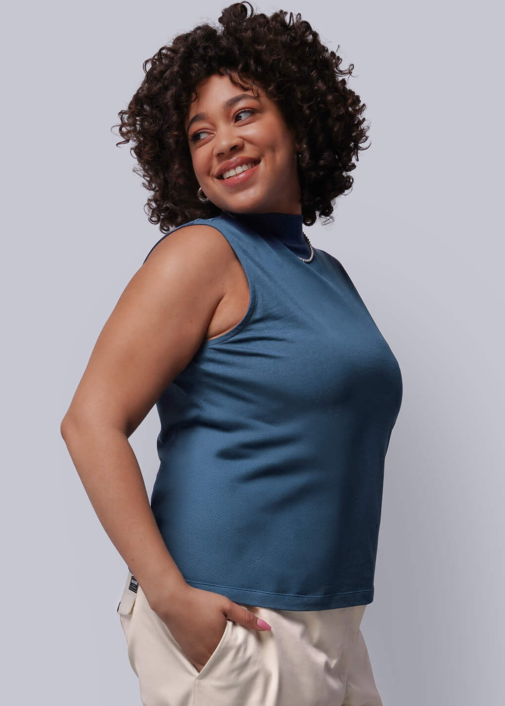 1X=Person wearing a blue sleeveless top and beige pants against a plain background