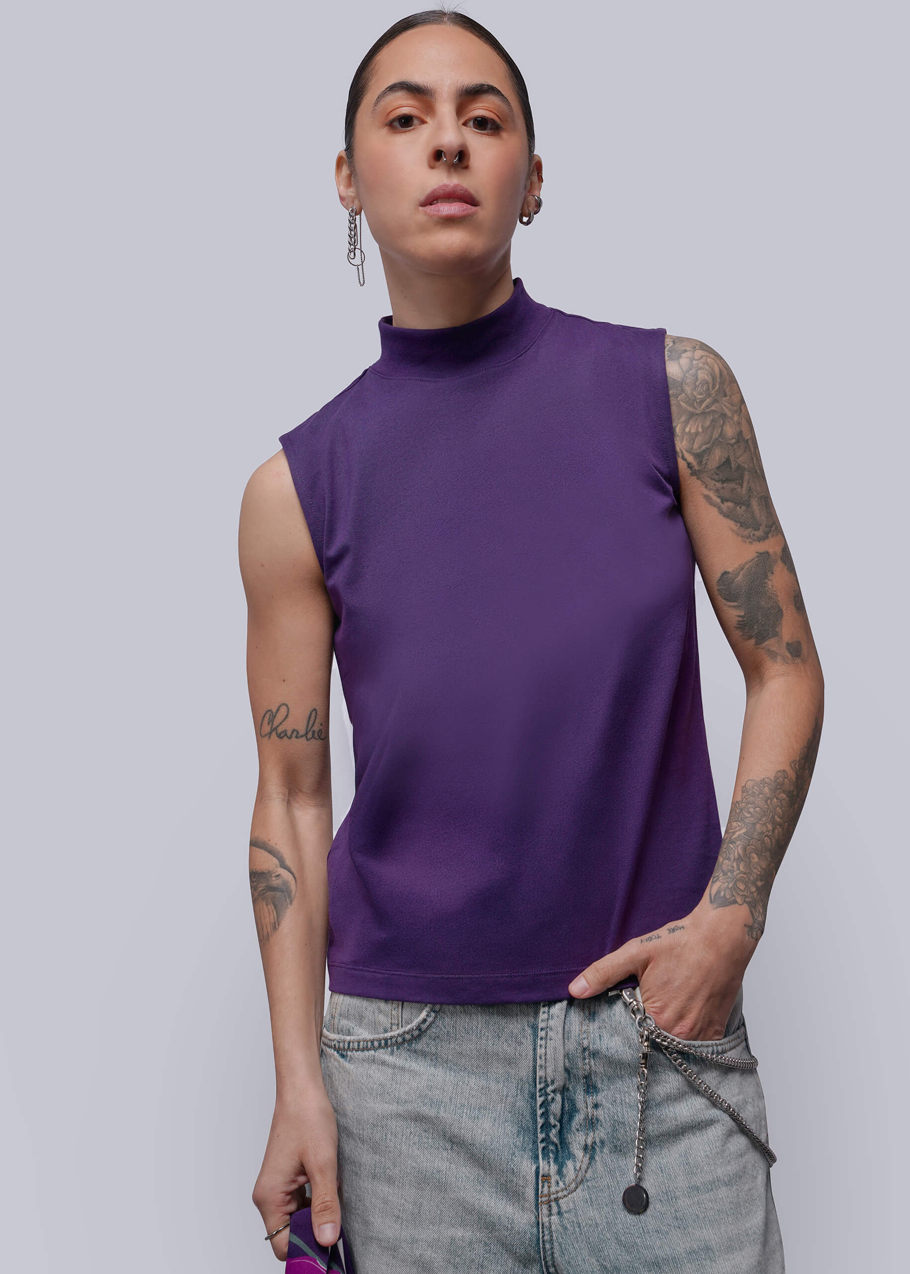 Person wearing a purple sleeveless top and jeans on a plain background