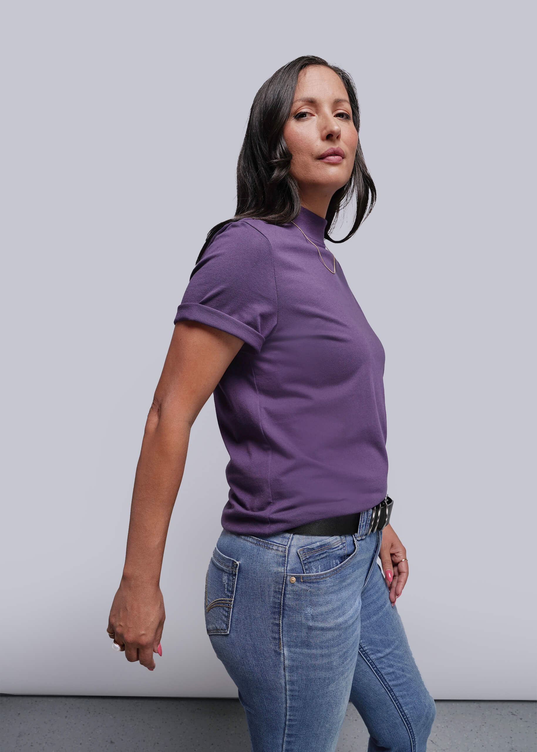 Woman wearing a purple shirt and blue jeans against a plain background