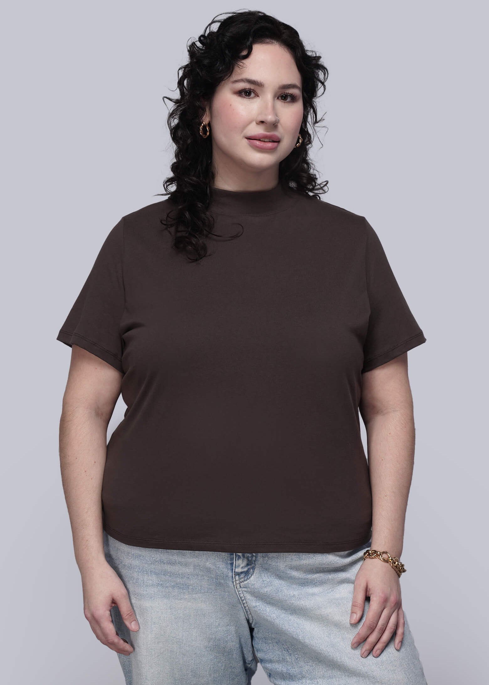 1X=Person wearing a brown t-shirt and light blue jeans against a plain background