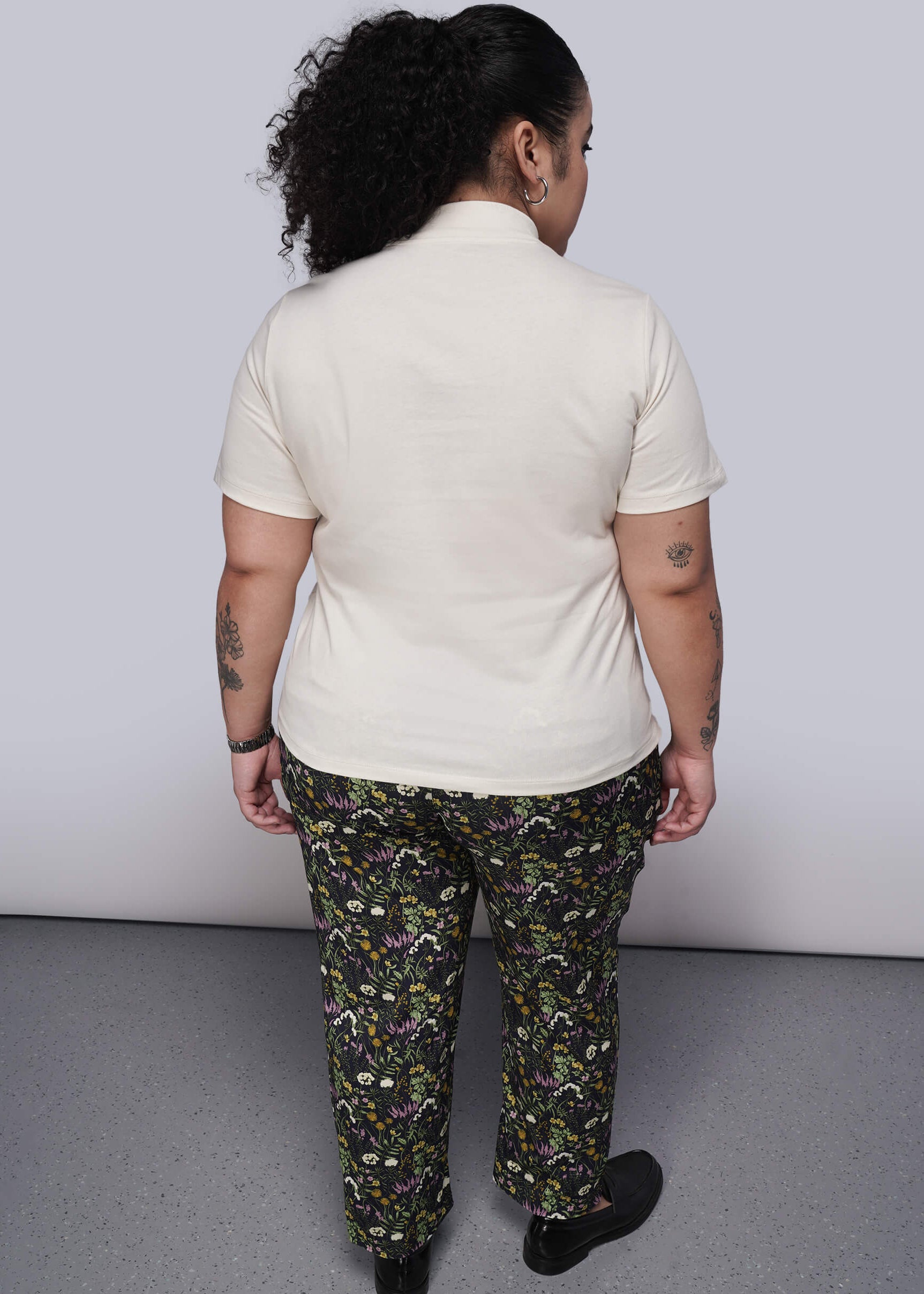 1X=Back of person wearing a white shirt and patterned pants against a plain background