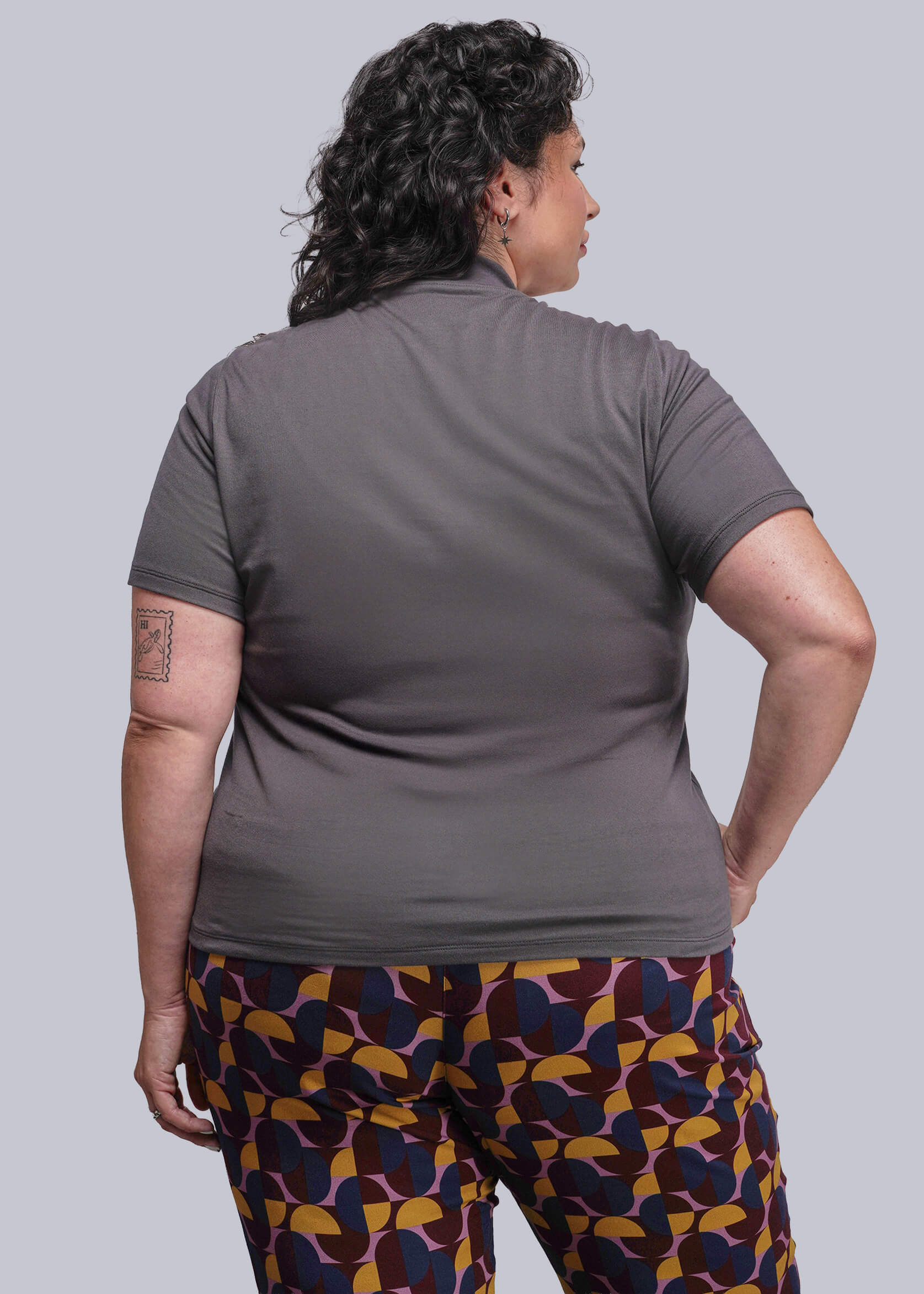 1X=Person wearing a gray shirt and patterned pants on a plain background